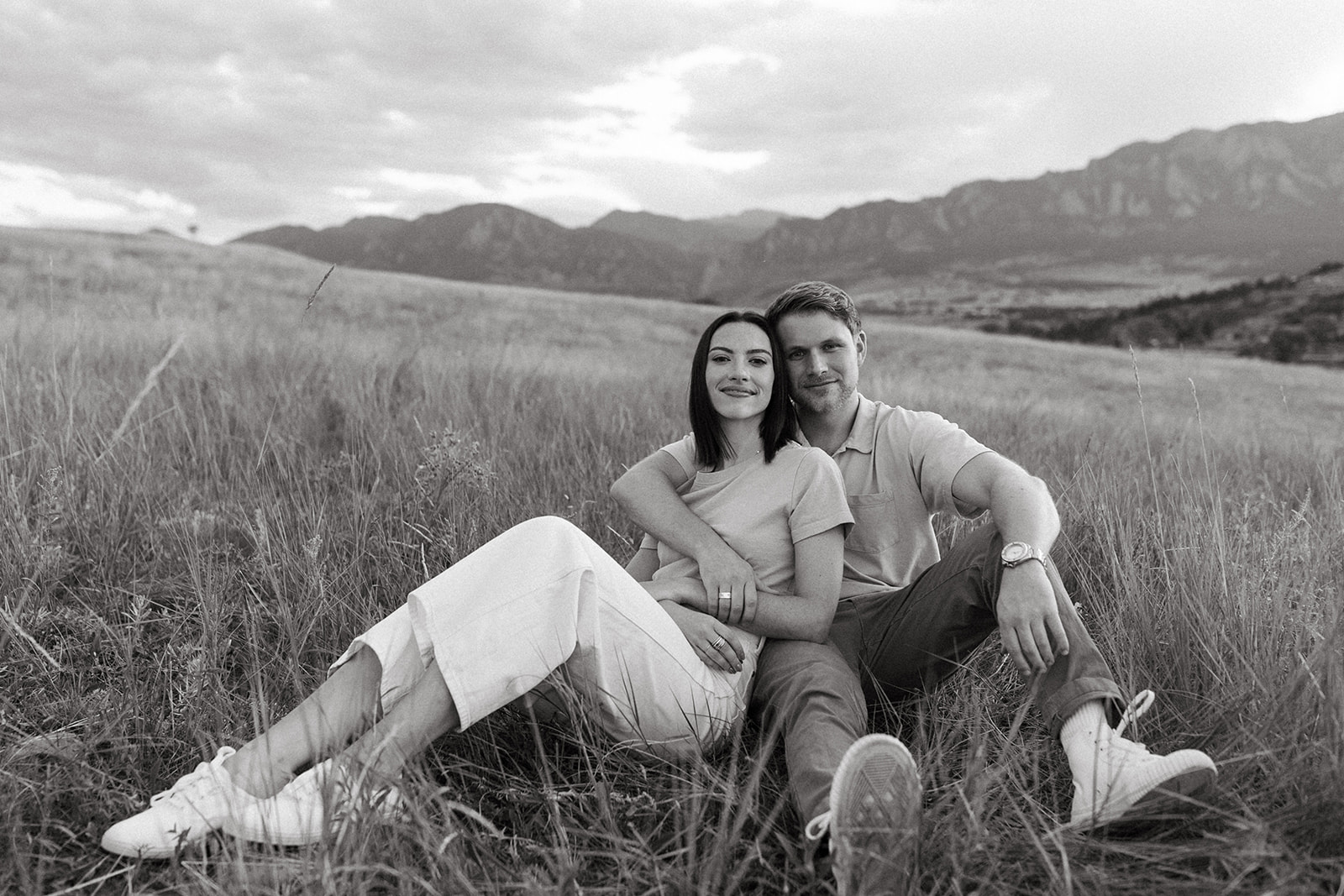A modern, fashion-forward engagement couple leans on one another while sitting in a meadow in Boulder, Colorado