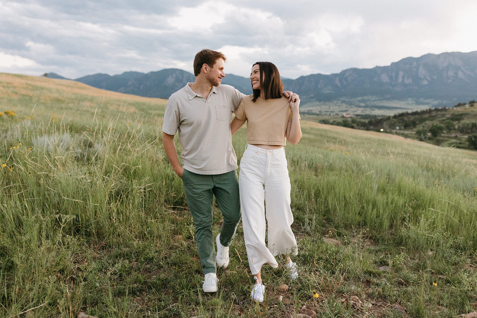 A man and woman walk through a wildflower meadow near The Flatirons in Boulder while taking editorial engagement photos