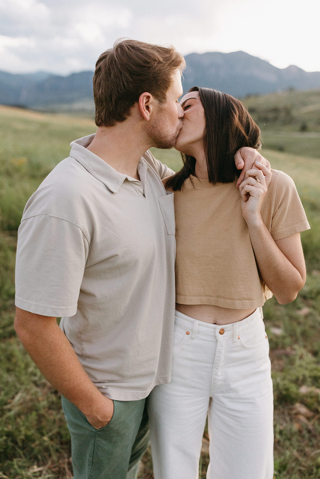 A modern, fashion-forward couple kisses while standing in a wildflower meadow in Boulder during an engagement session