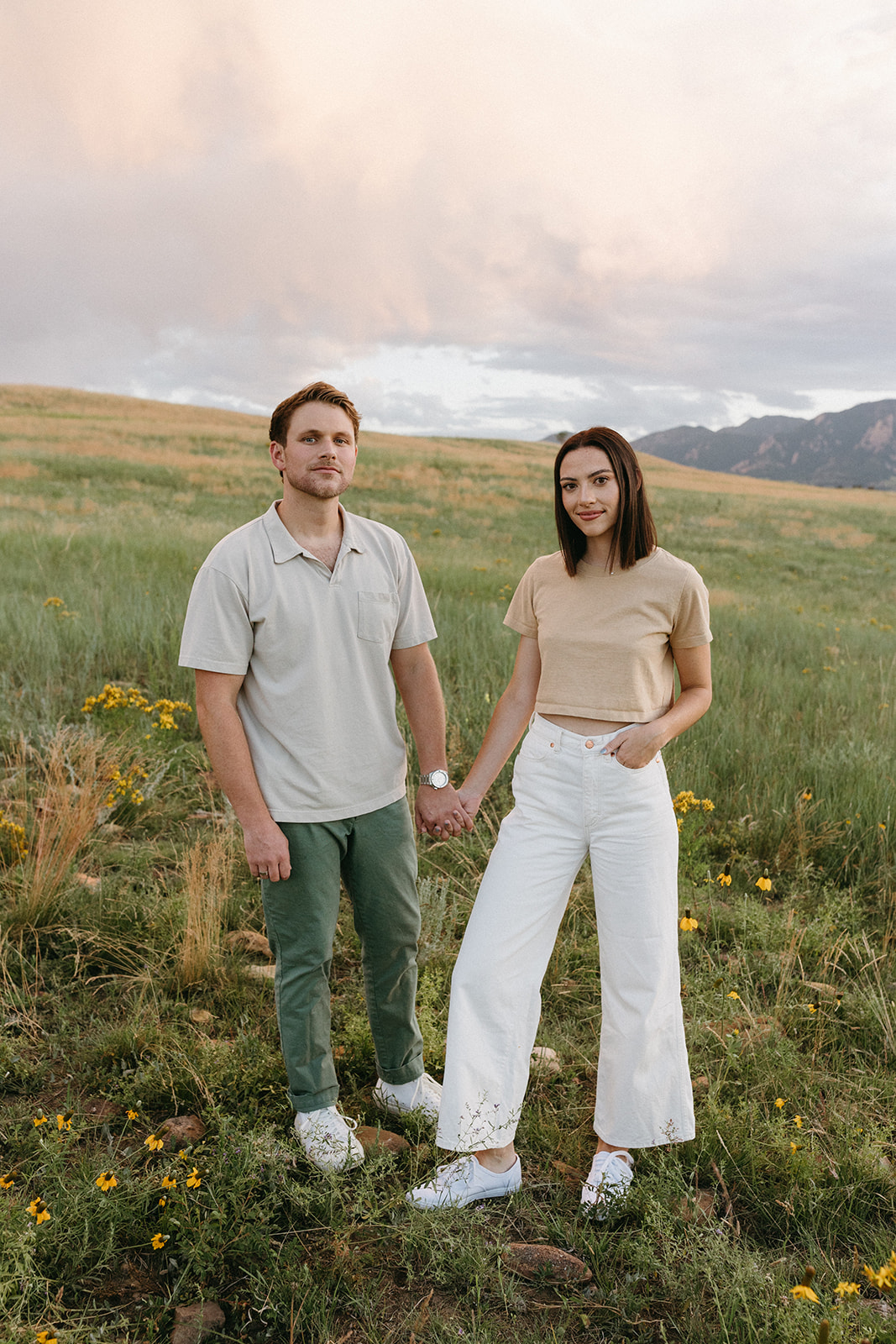 A Colorado engagement session couple holds hands while smiling in a wildflower meadow at Sunset in Boulder