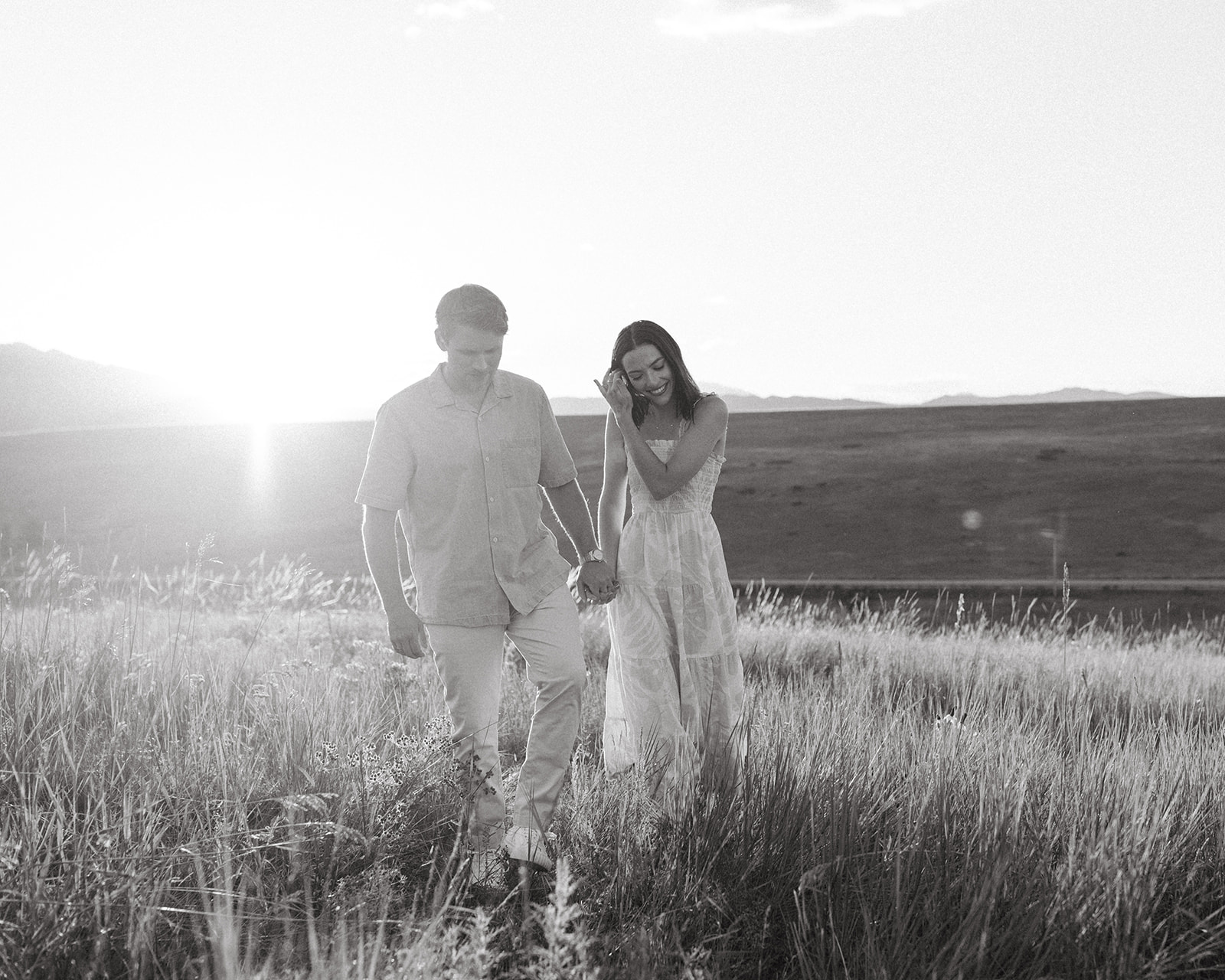 A man and woman walk through a field in Boulder while taking editorial engagement photos near The Flatirons