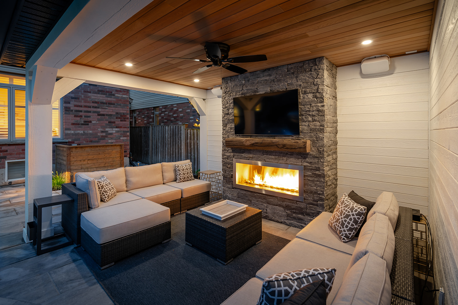 Two outdoor couches underneath a gazebo with a TV and fireplace on the wall.