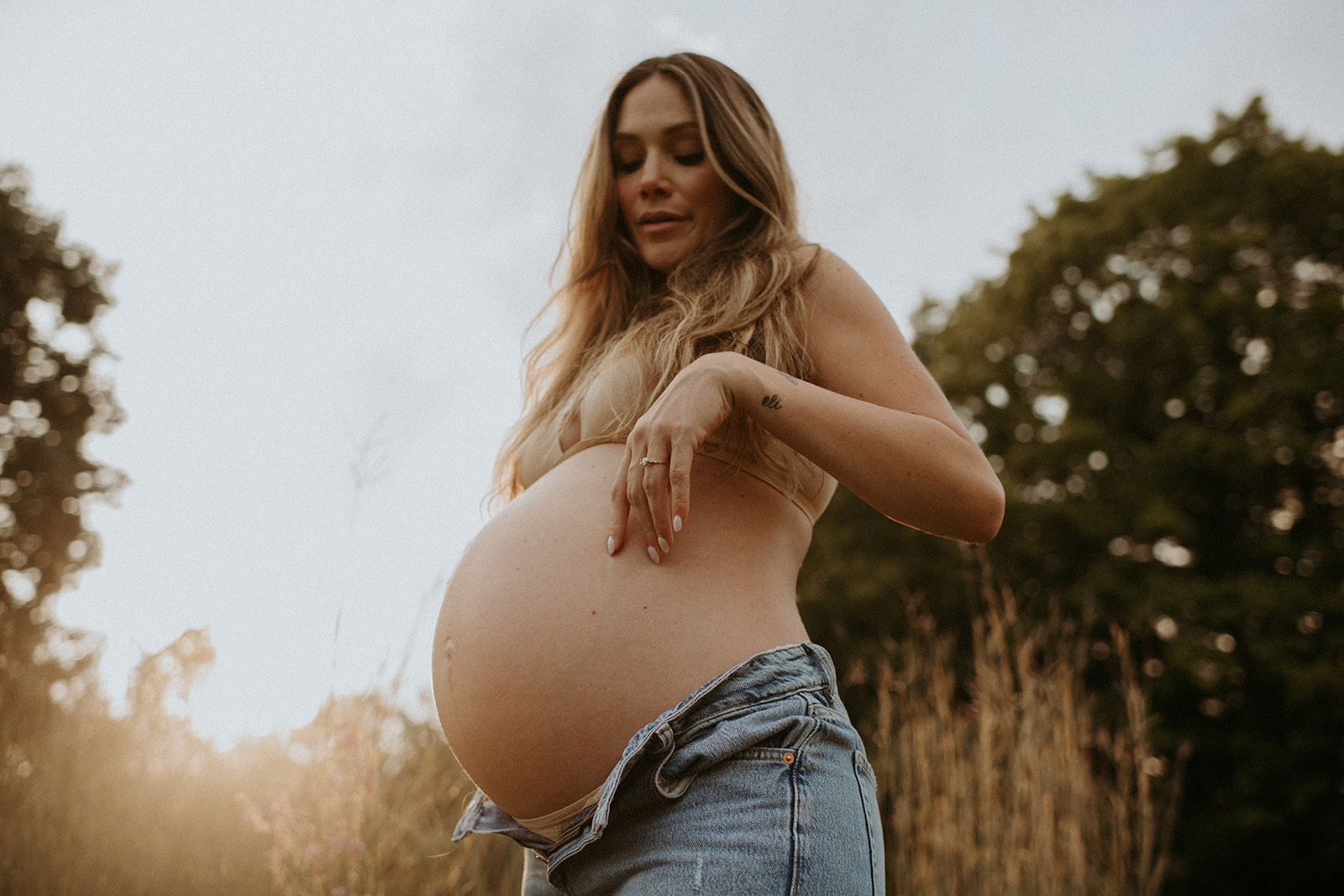 Beautiful mom-to-be poses for maternity photos in unbuttoned jeanse