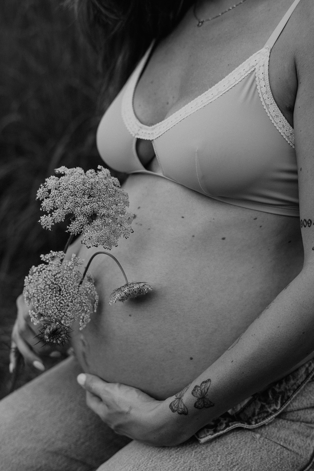 Detail shot of a pregnant mother holding flowers next to her belly during her outdoor maternity photoshoot