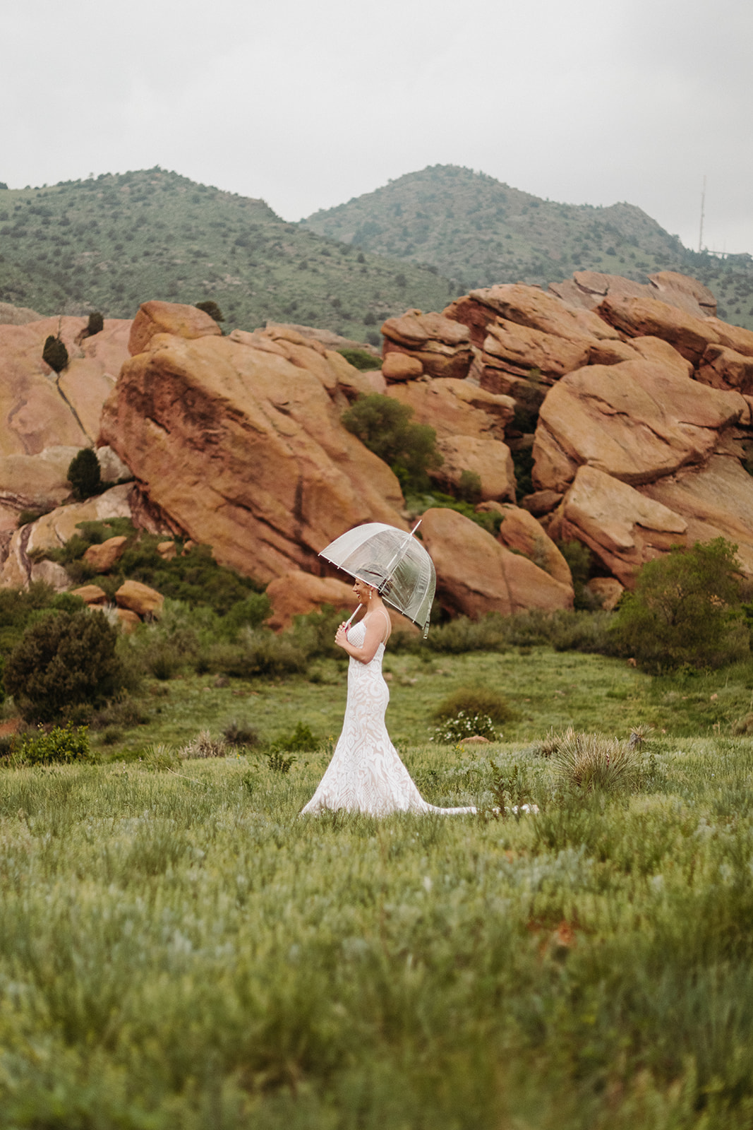 Bridal portrait at red rocks in the rain as the bride holds a clear umbrella.