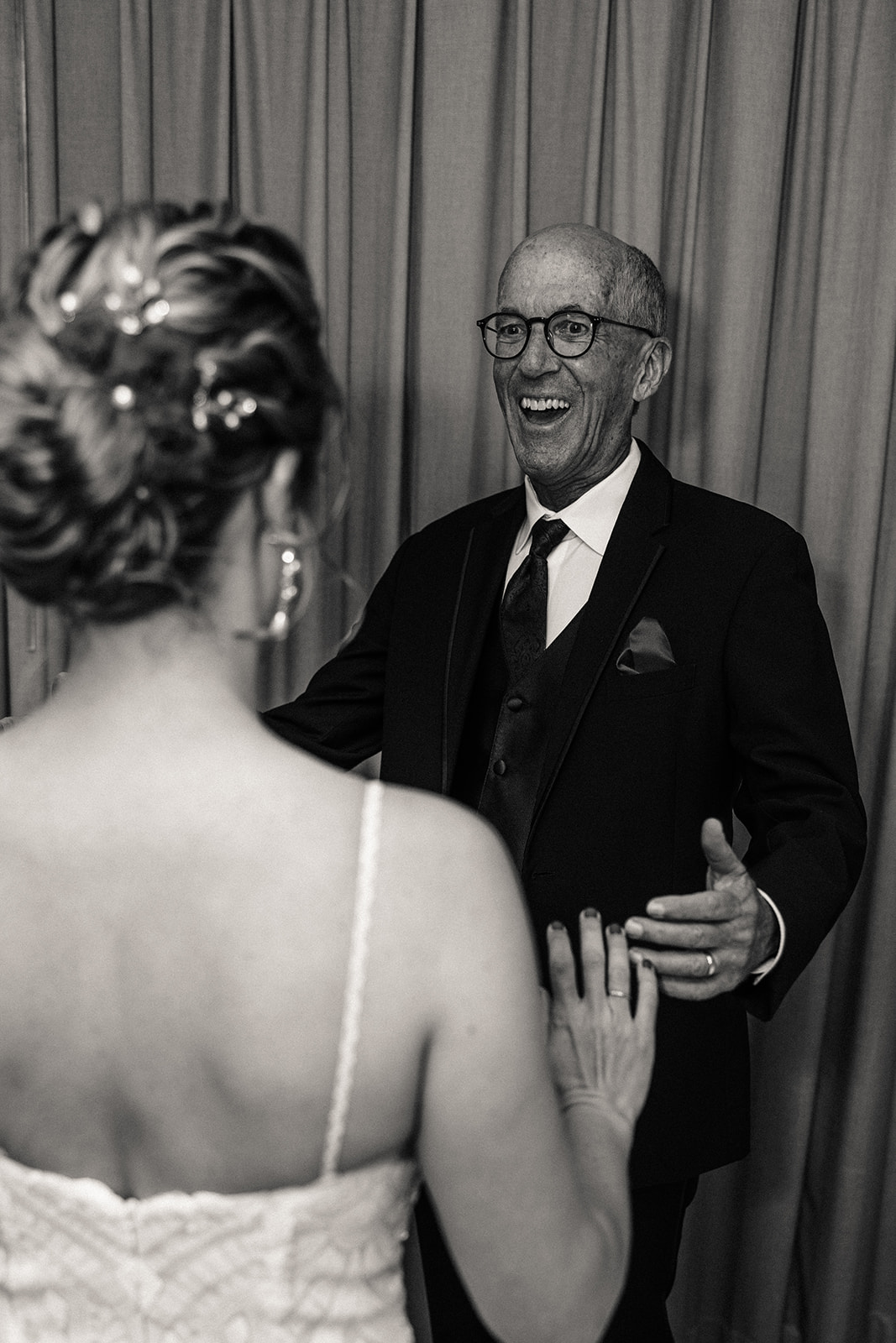 The father of the bride seeing his daughter in her wedding dress for the first time, smiling ear-to-ear.