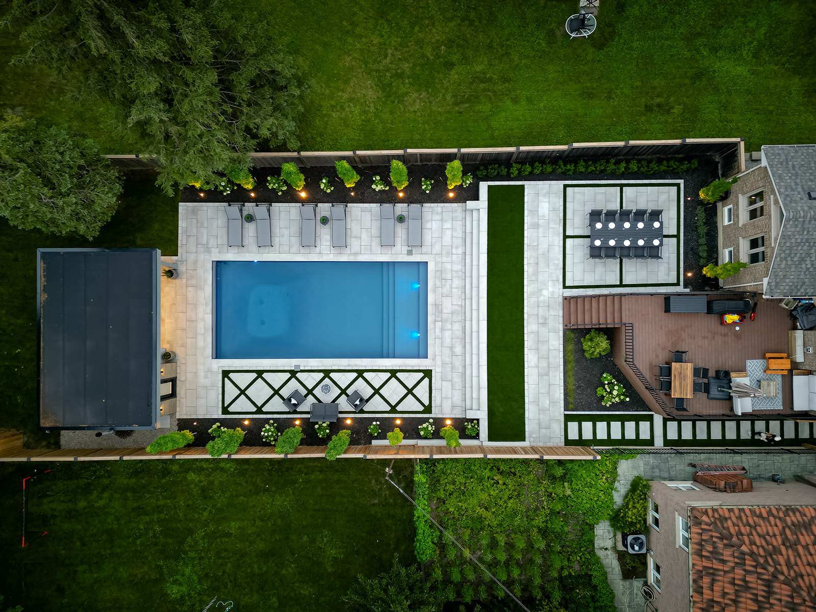 Top-down view of an inground pool, lounge chairs, a pool house and a deck beside the house.