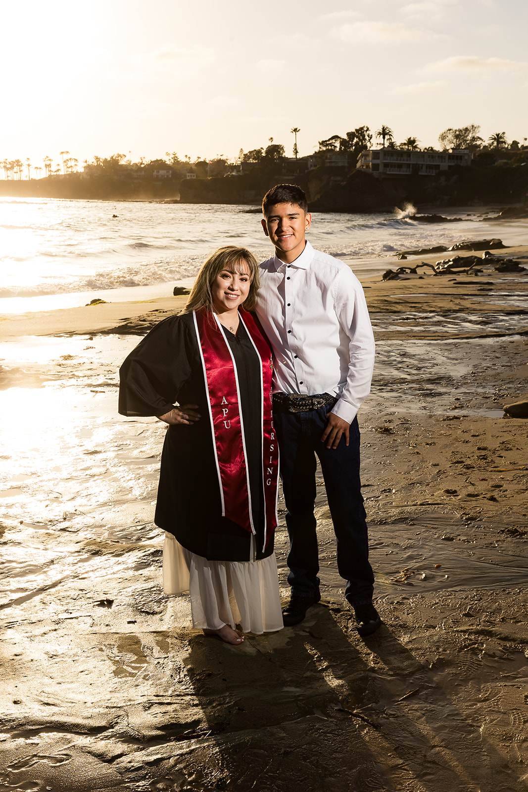 mom in graduation regalia at the beach with her son