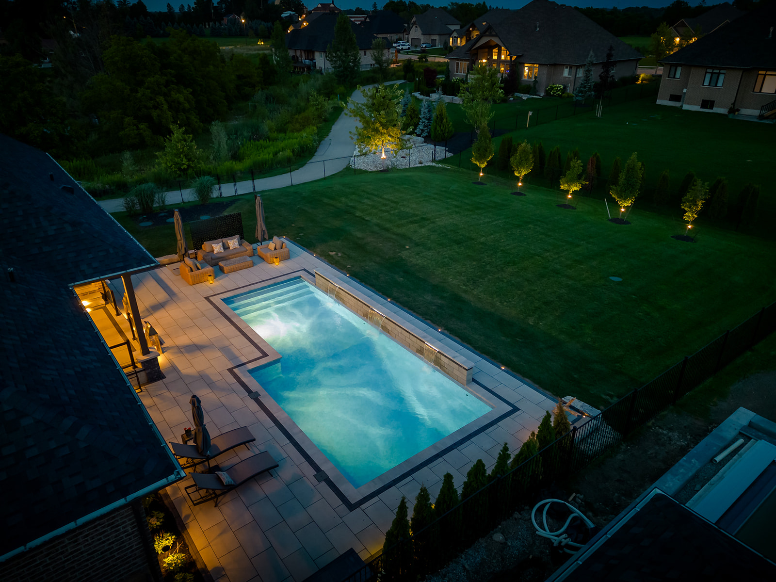 An inground pool with lights on in the water and on the house.