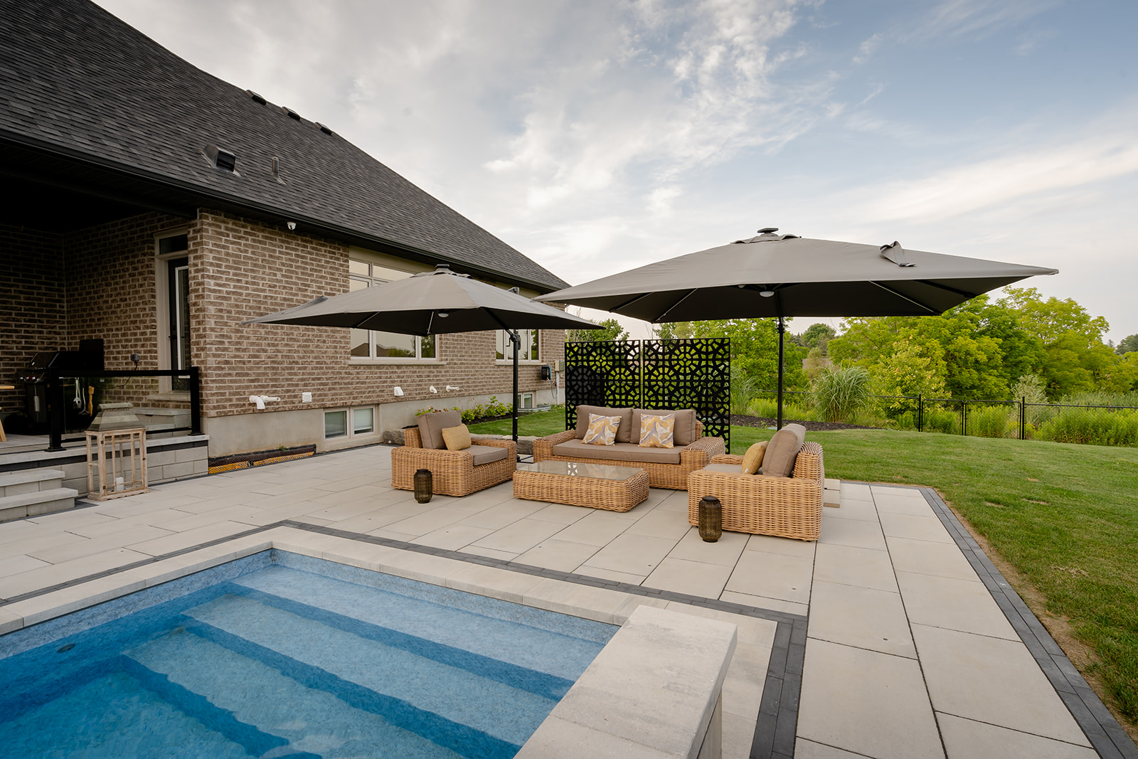 An outdoor seating area with both umbrellas open and an inground pool in front.