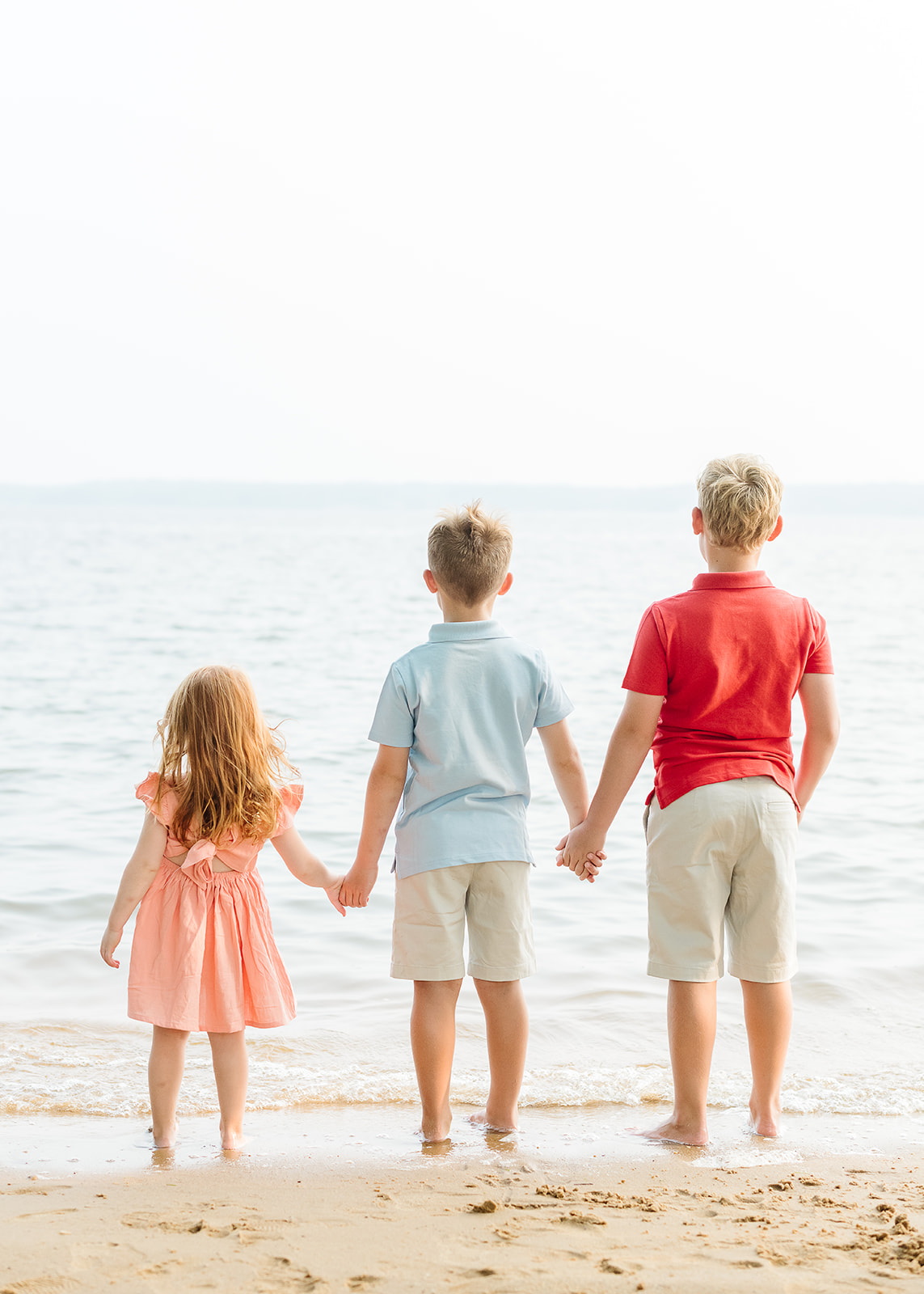 three siblings hold hands while starting out at the water at Patuxent River for a family photo session in Maryland 