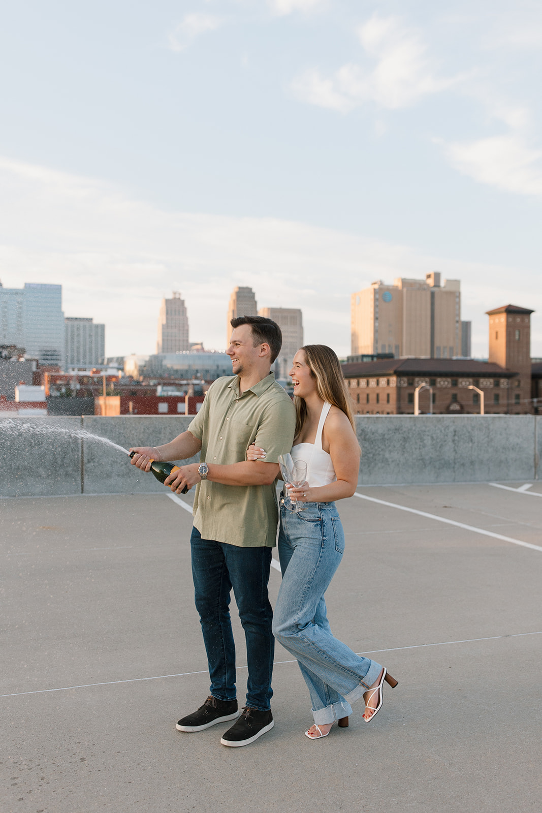 a couple pops champagne on a rooftop in downtown Kansas City for their engagement photoshoot
