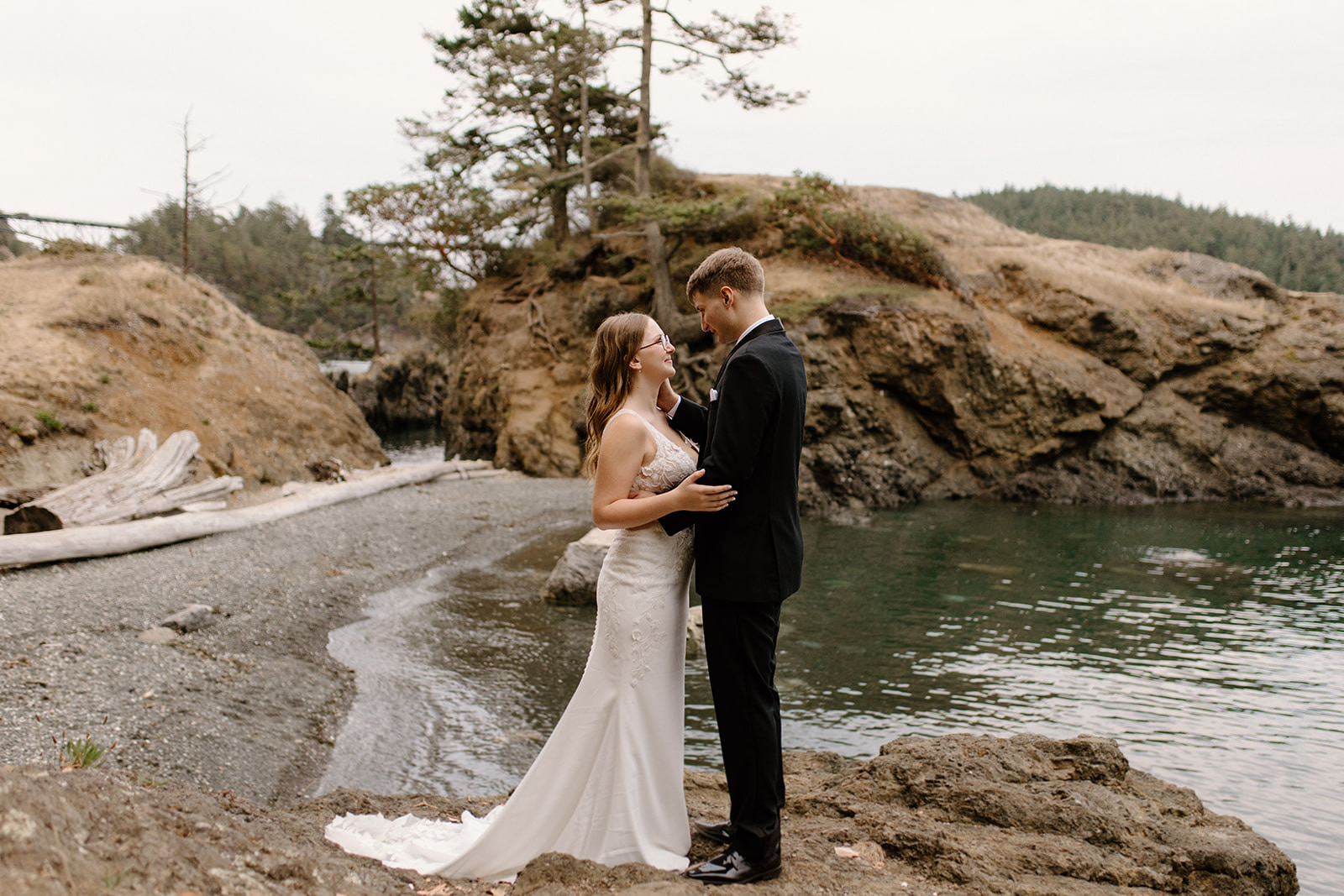 A forested, coastal photoshoot with a couple in their wedding attire at Deception Pass in Washington state.