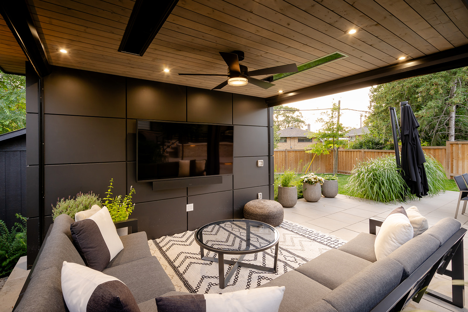 An outdoor patio set with cushions on underneath the gazebo with a tv on the wall.