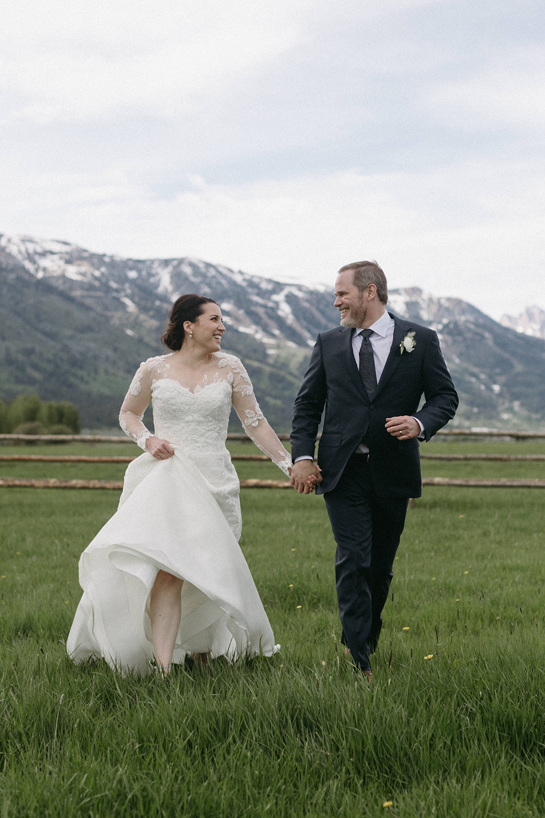 A bride and groom in elegant wedding attire run through a meadow at Snake River Ranch in Wyoming. 