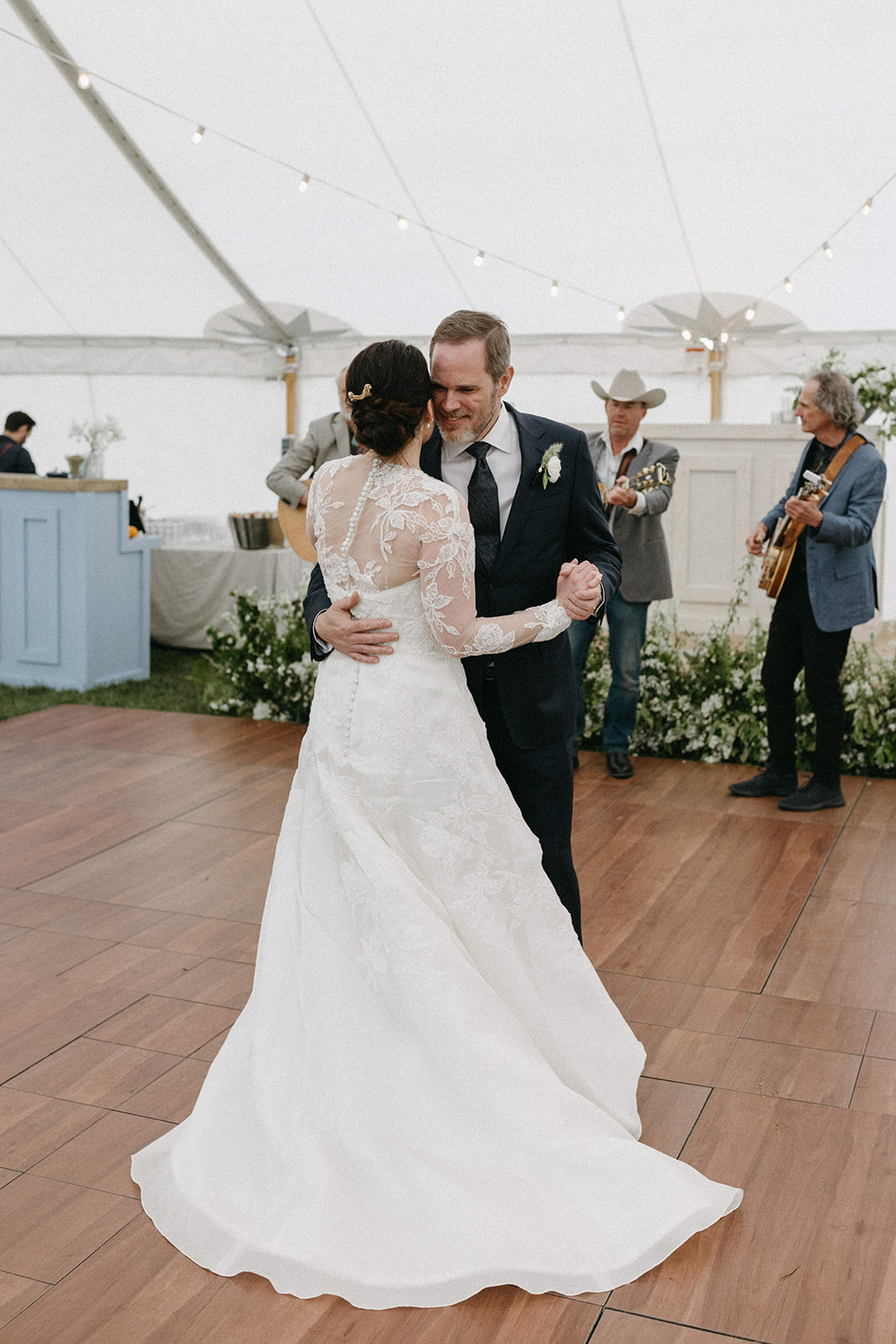 A couple shares their first dance while a live band plays in the background during their ranch wedding reception. 
