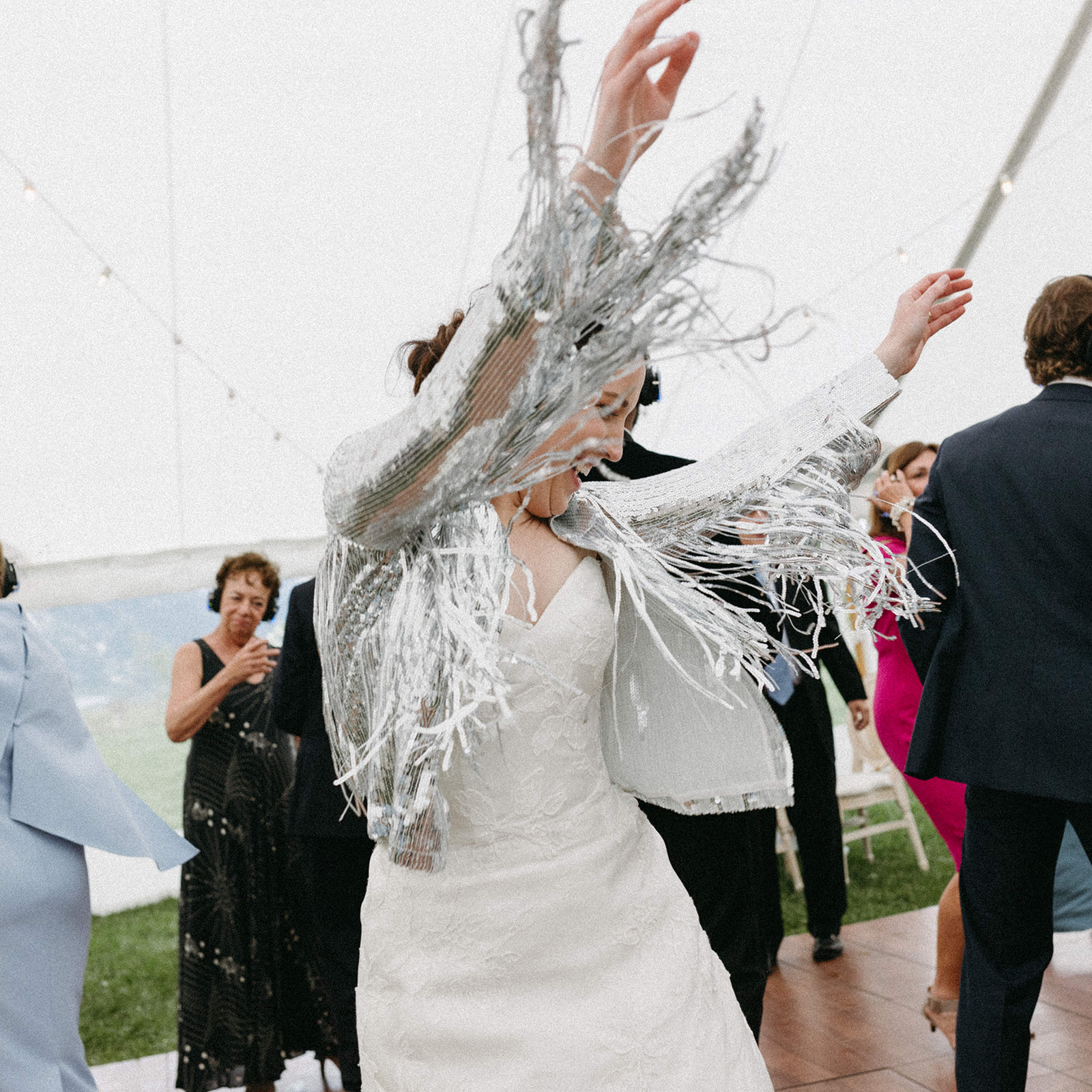 A bride, wearing a silver-sequin fringe jacket, dances at a silent disco wedding reception with guests. 