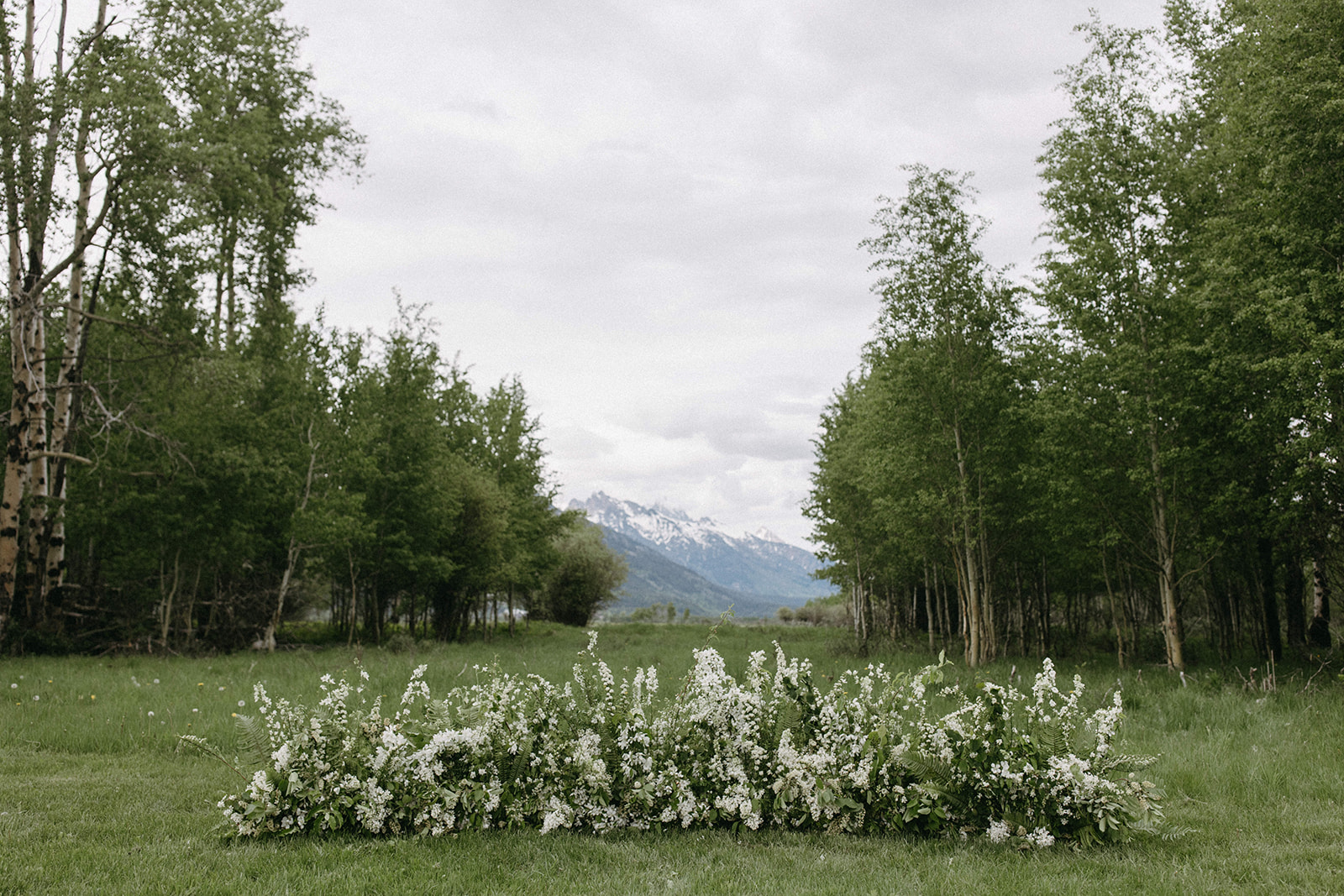 A grounded white floral arch in a ranch meadow near the Tetons in Jackson Hole, Wyoming. 
