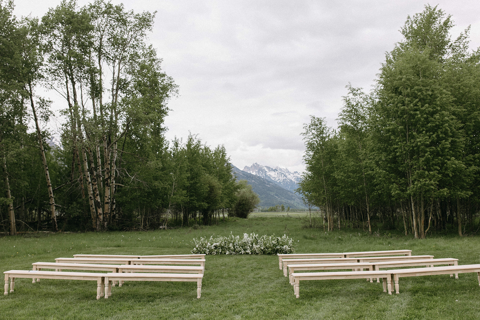 A grounded floral arch at the end of an outdoor wedding ceremony aisle with snowy mountains in the distance. 
