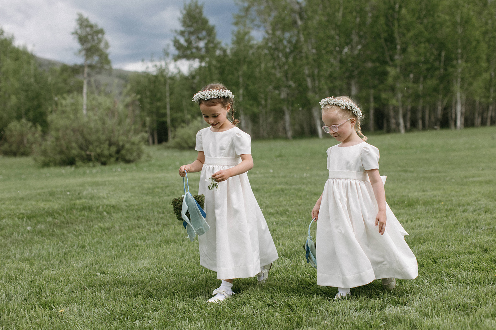Two flower girls spread pedals down the aisle while wearing white flower girl dresses and white flower crowns. 