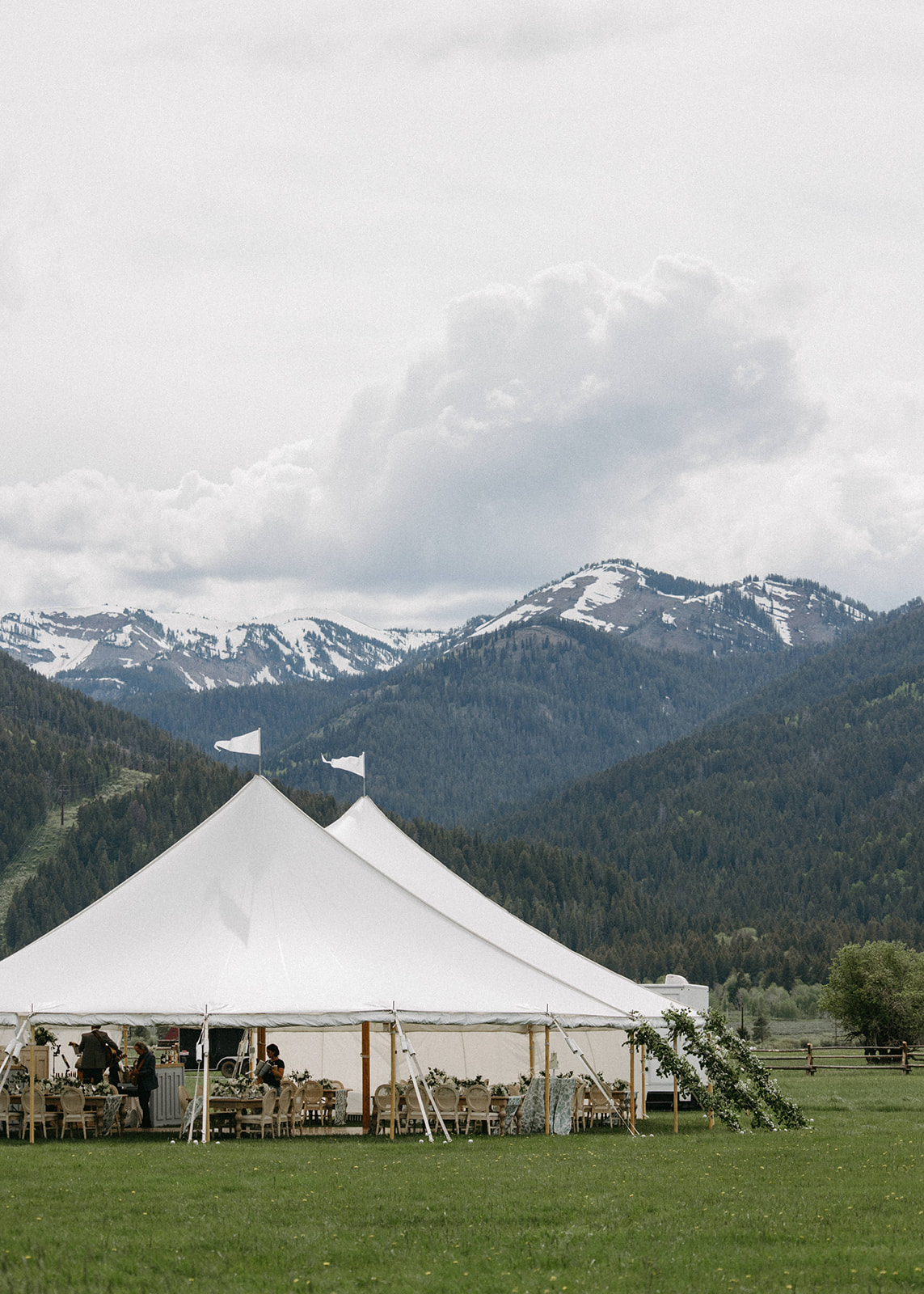 A white, outdoor luxury wedding reception tent in a meadow. 

