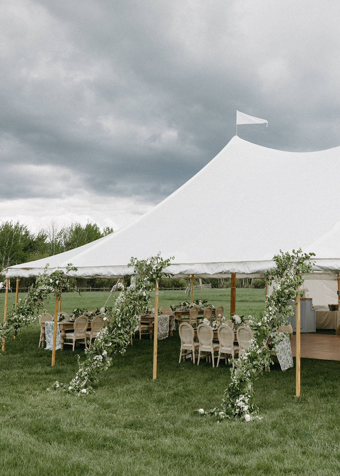 A white, outdoor wedding reception tent in a meadow decorated with white flowers. 