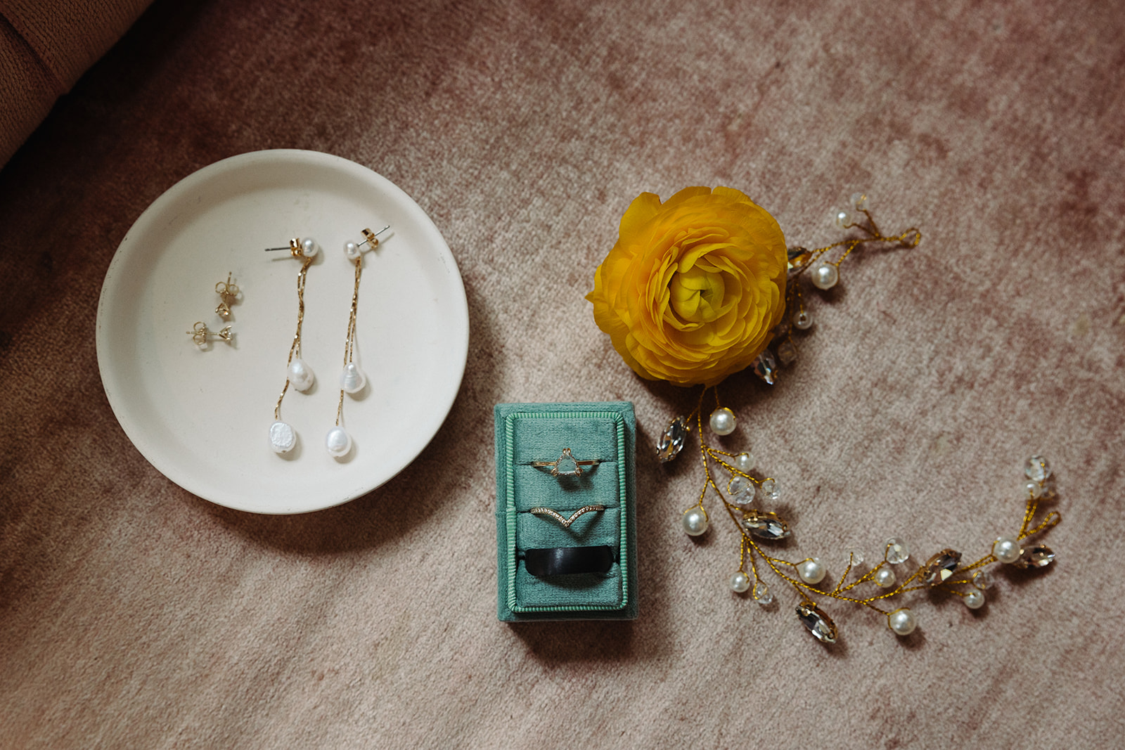 A close-up of the couple's accessories, including pearl dangling earrings, gold studs, hair brooch, and a teal ring box.