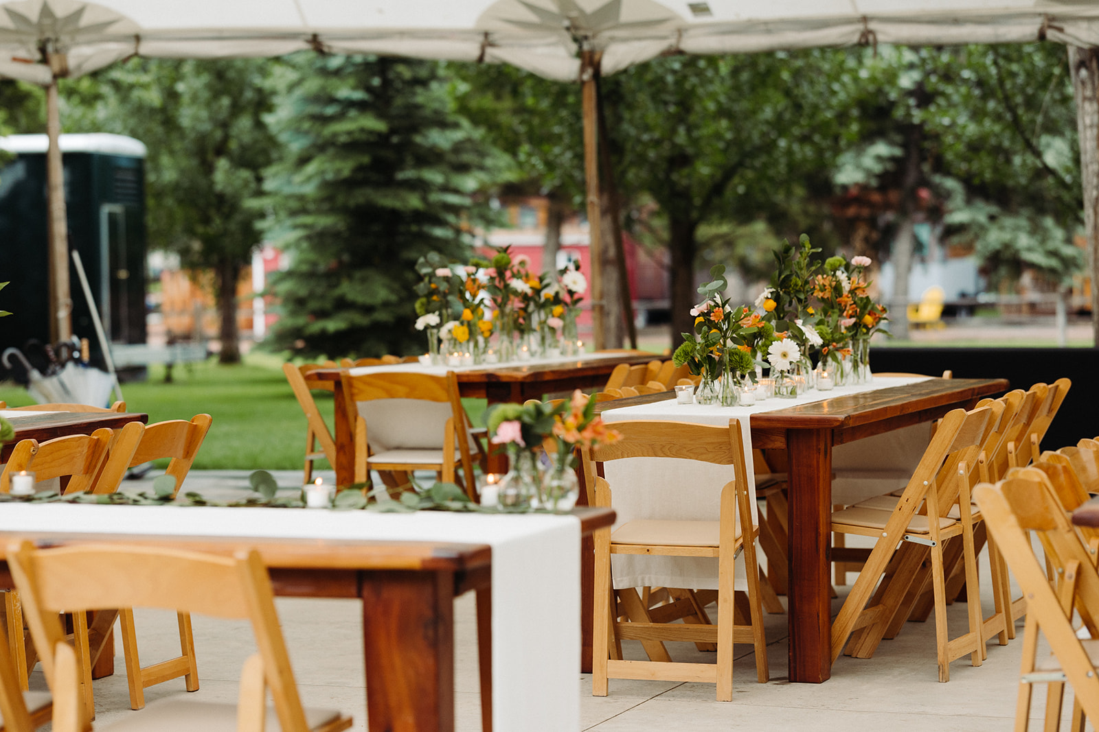 The tented reception at River Bend, complete with wooden tables that are decorated with bright orange and white flowers.