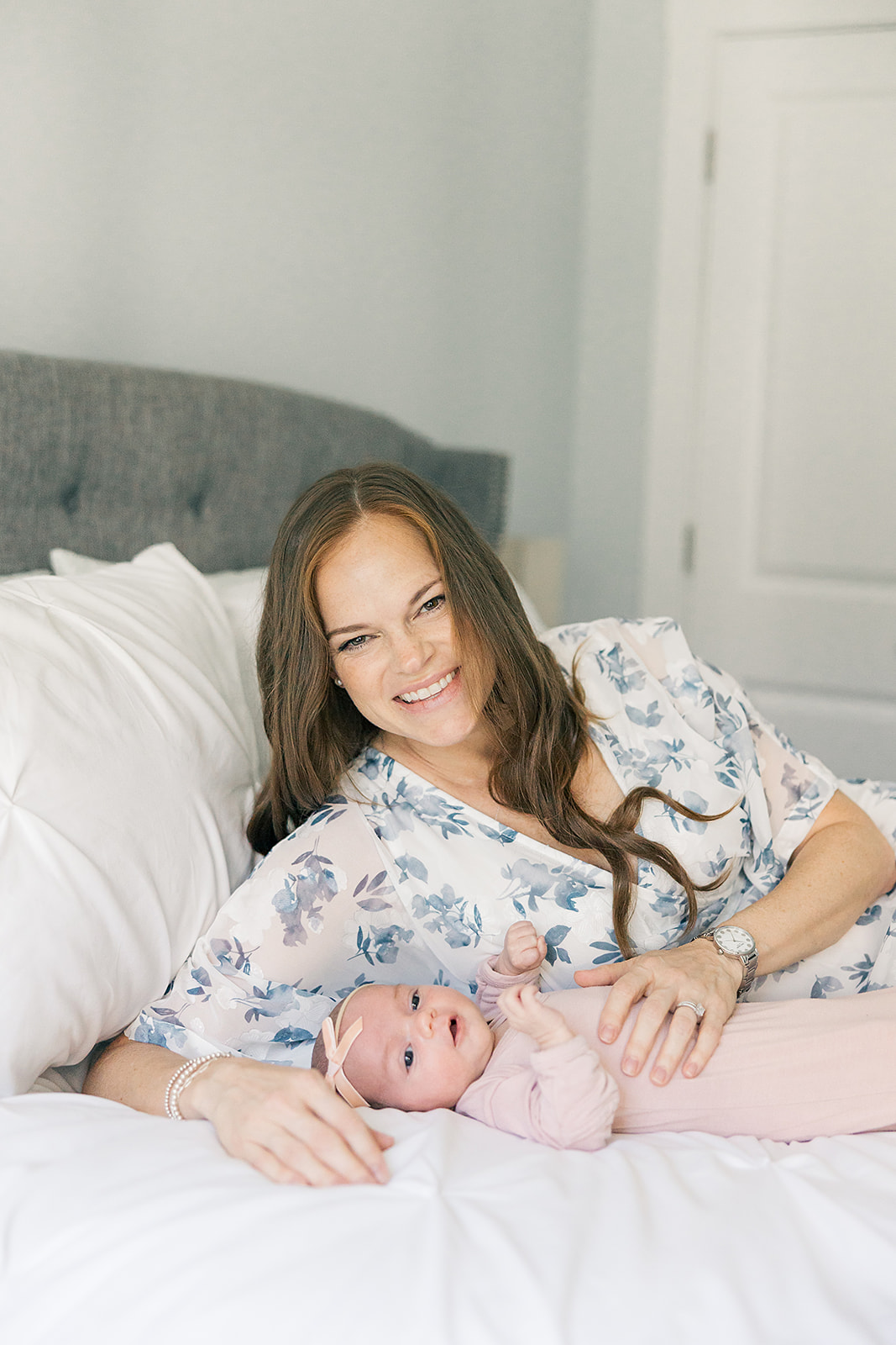 mom snuggled with newborn baby girl on white bed