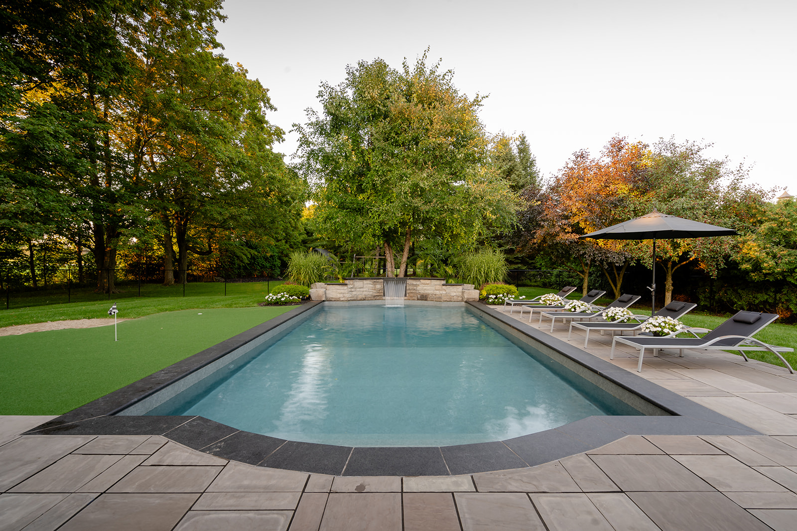 An inground pool with lawn chairs on the right of the pool.