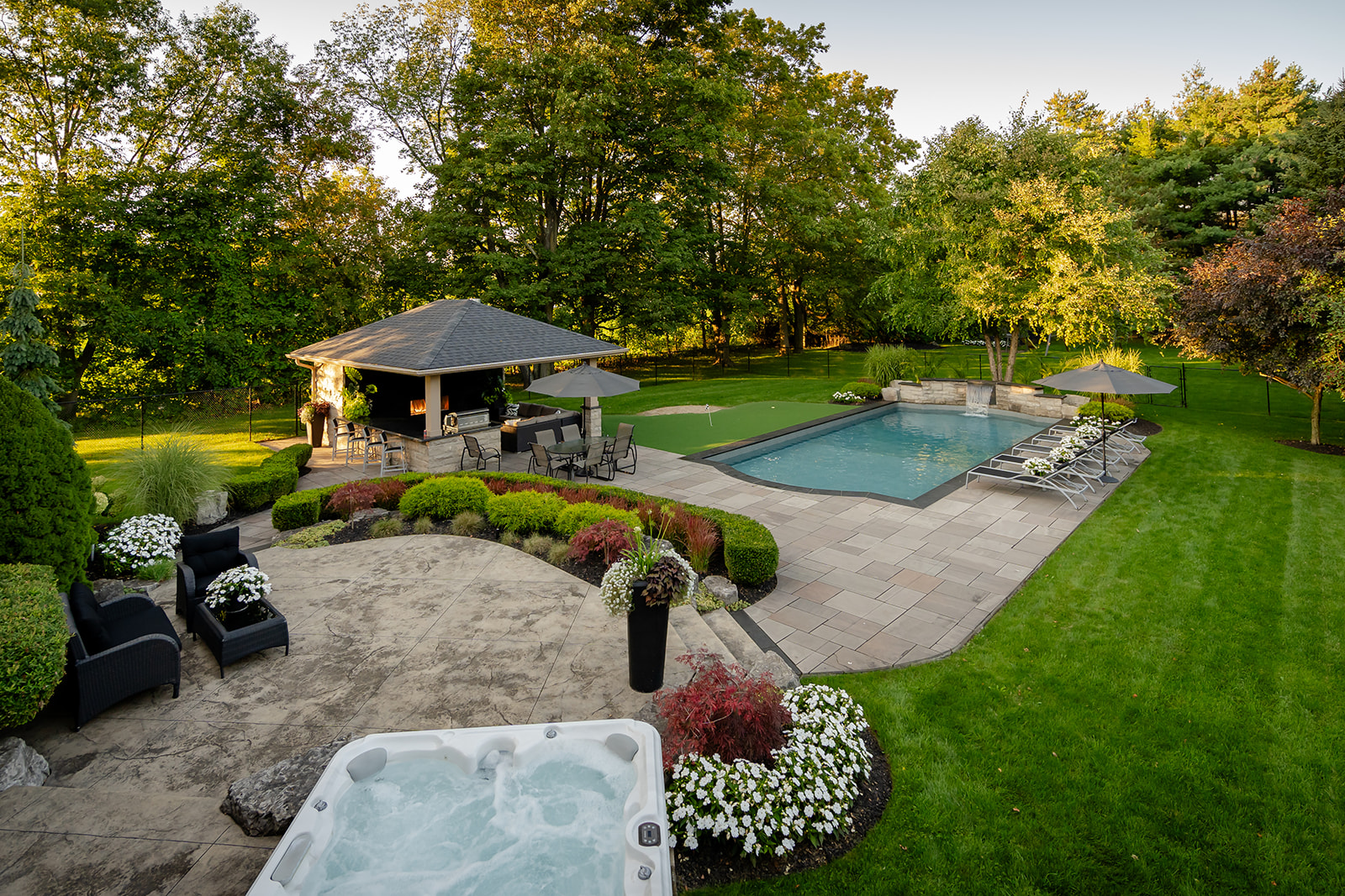 An inground pool with a mini waterfall flowing into it with lawn chairs on the right.