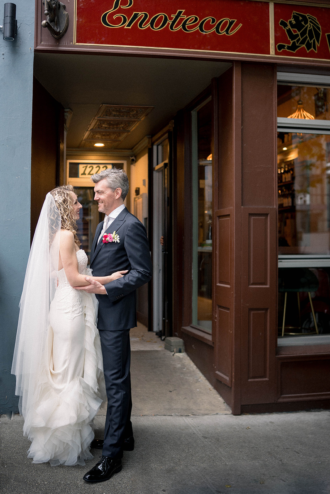 bride and groom kiss against a door in front of sole repair shop