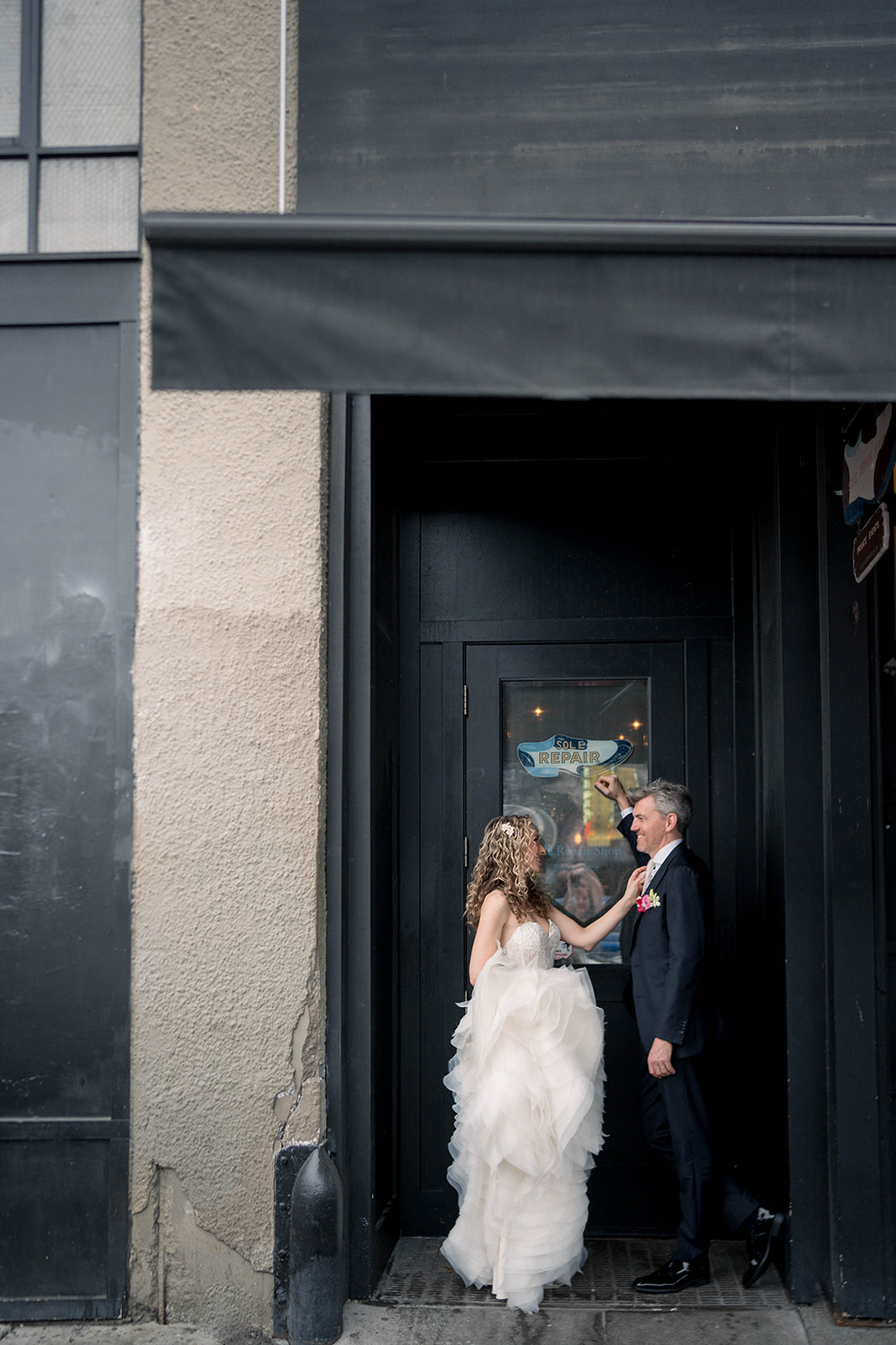 bride and groom hold each other in front of sole repair shop