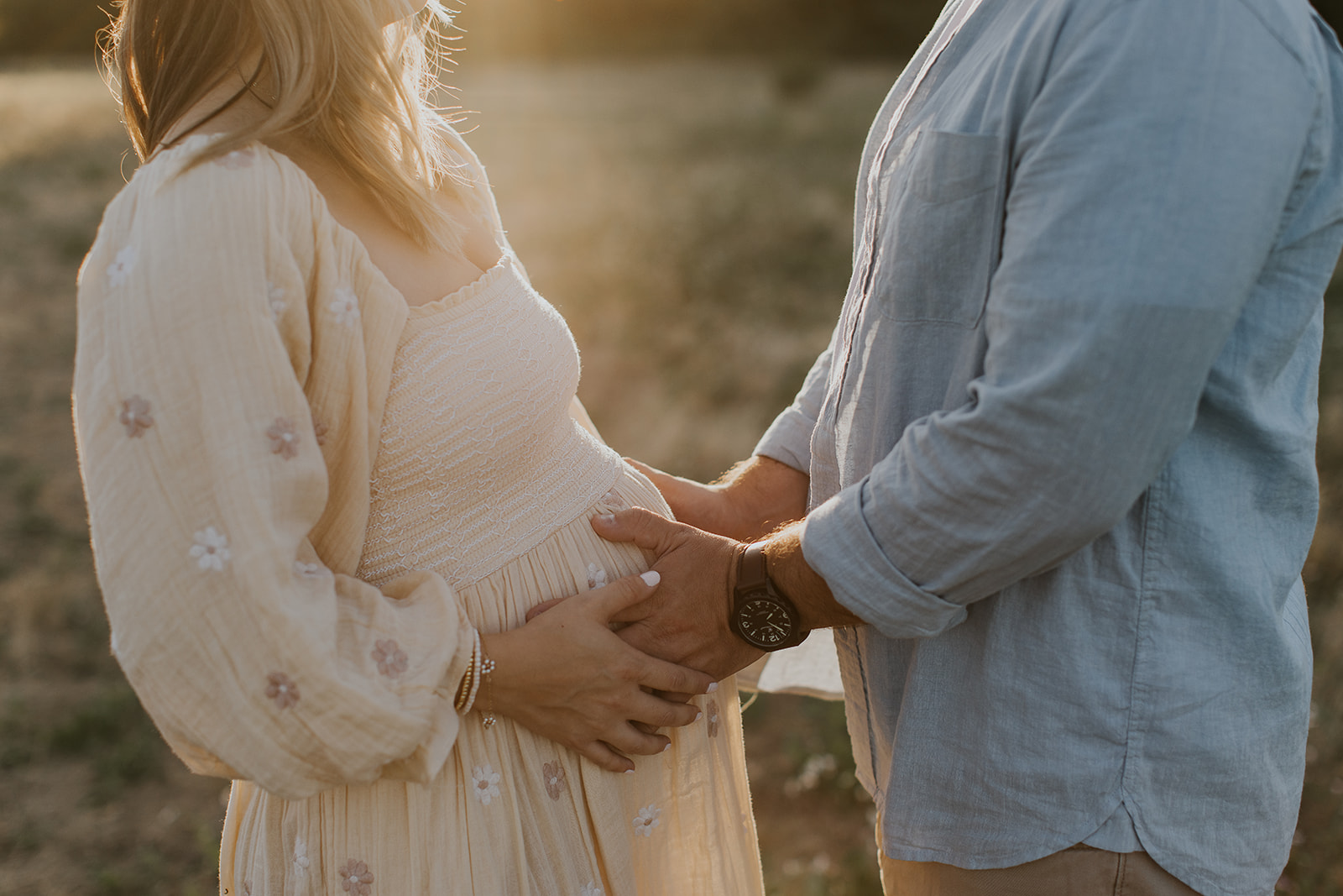 an expecting couple holding the baby bump with the sun shining through
