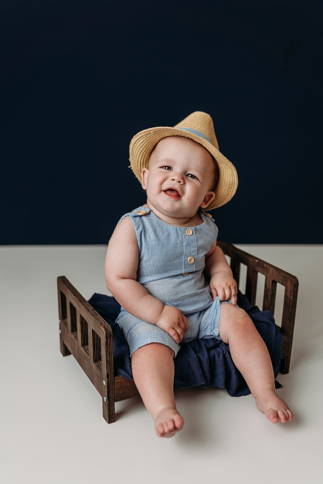 Cute baby sits on little wooden bed during photo shoot with Heather Ann Photography