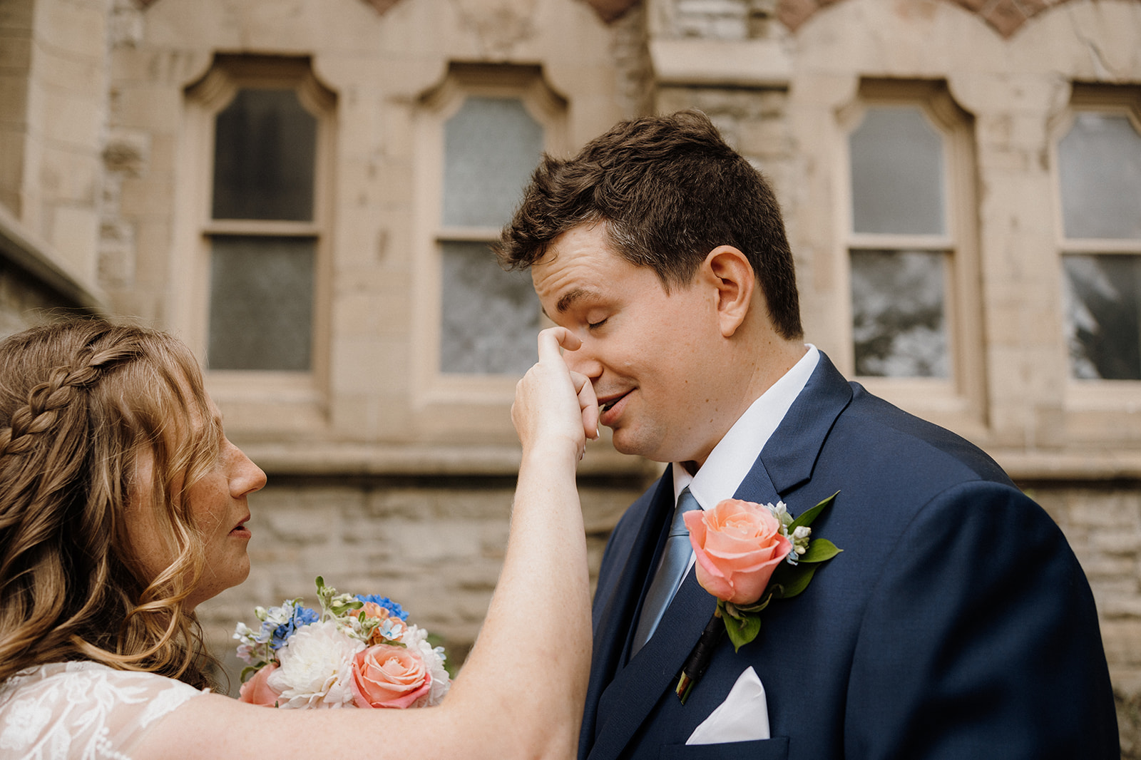 A bride wiping tears away on grooms face.