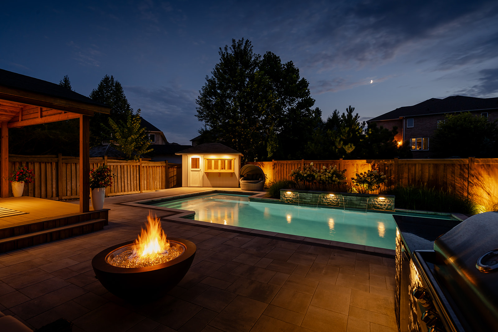 An inground pool with the fireplace on and lights.