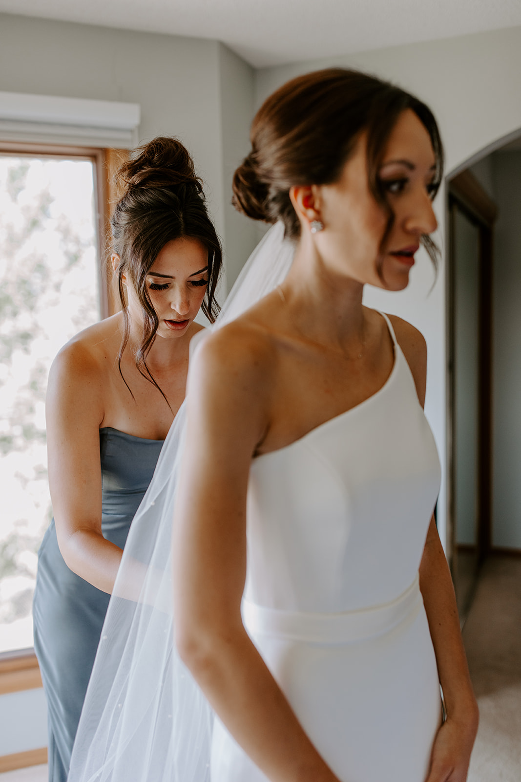 bride having her dress done up by bridesmaid 