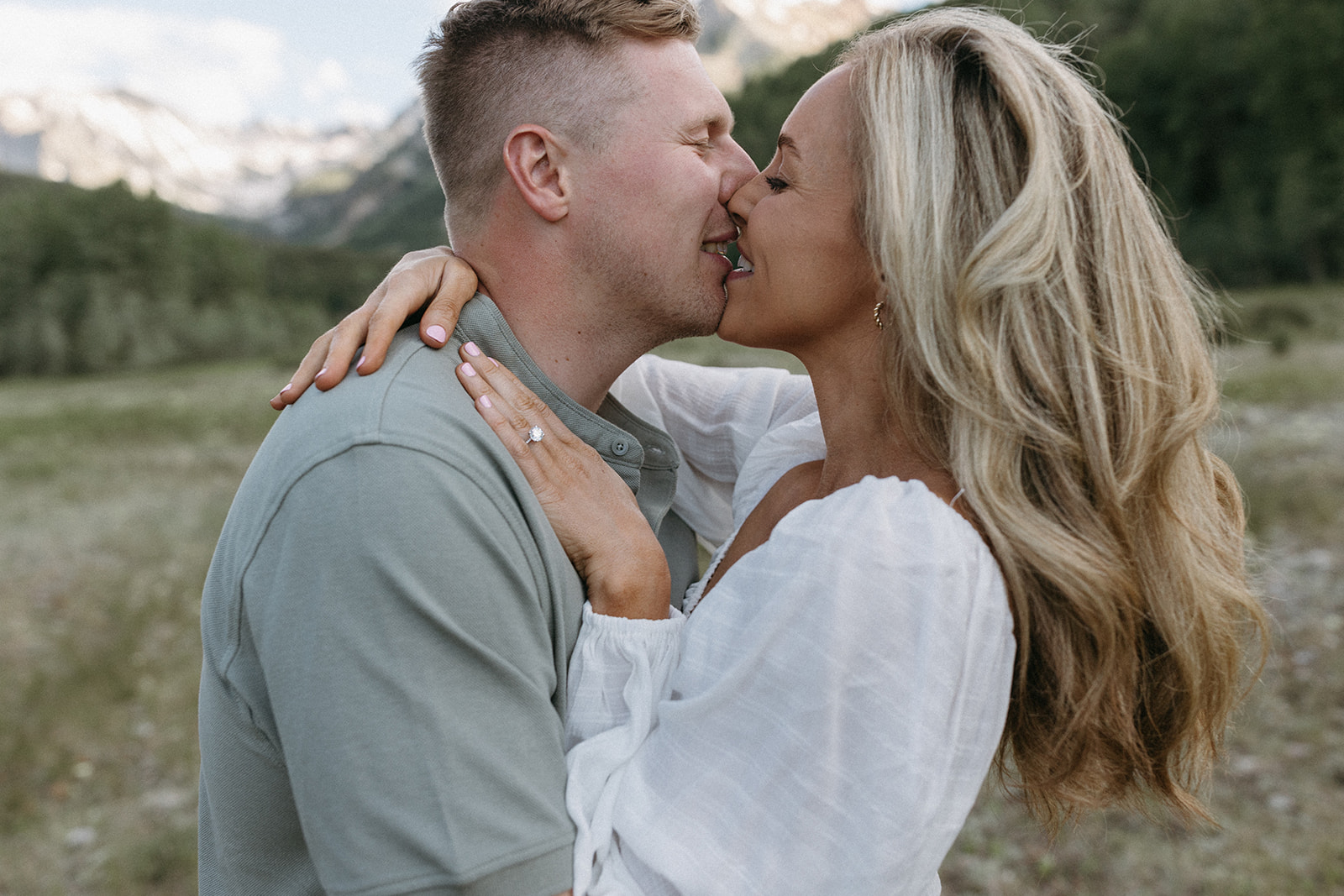 An engaged couple kisses in an Aspen wildflower meadow wearing neutral, earthy-toned engagement outfits. 