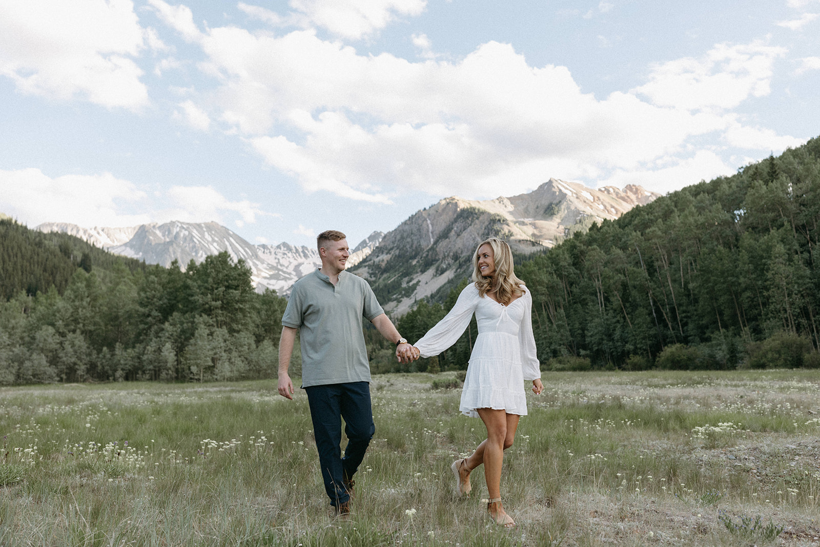 An engaged couple holds hands in a wildflower meadow during an Aspen engagement session in the Rocky Mountains. 