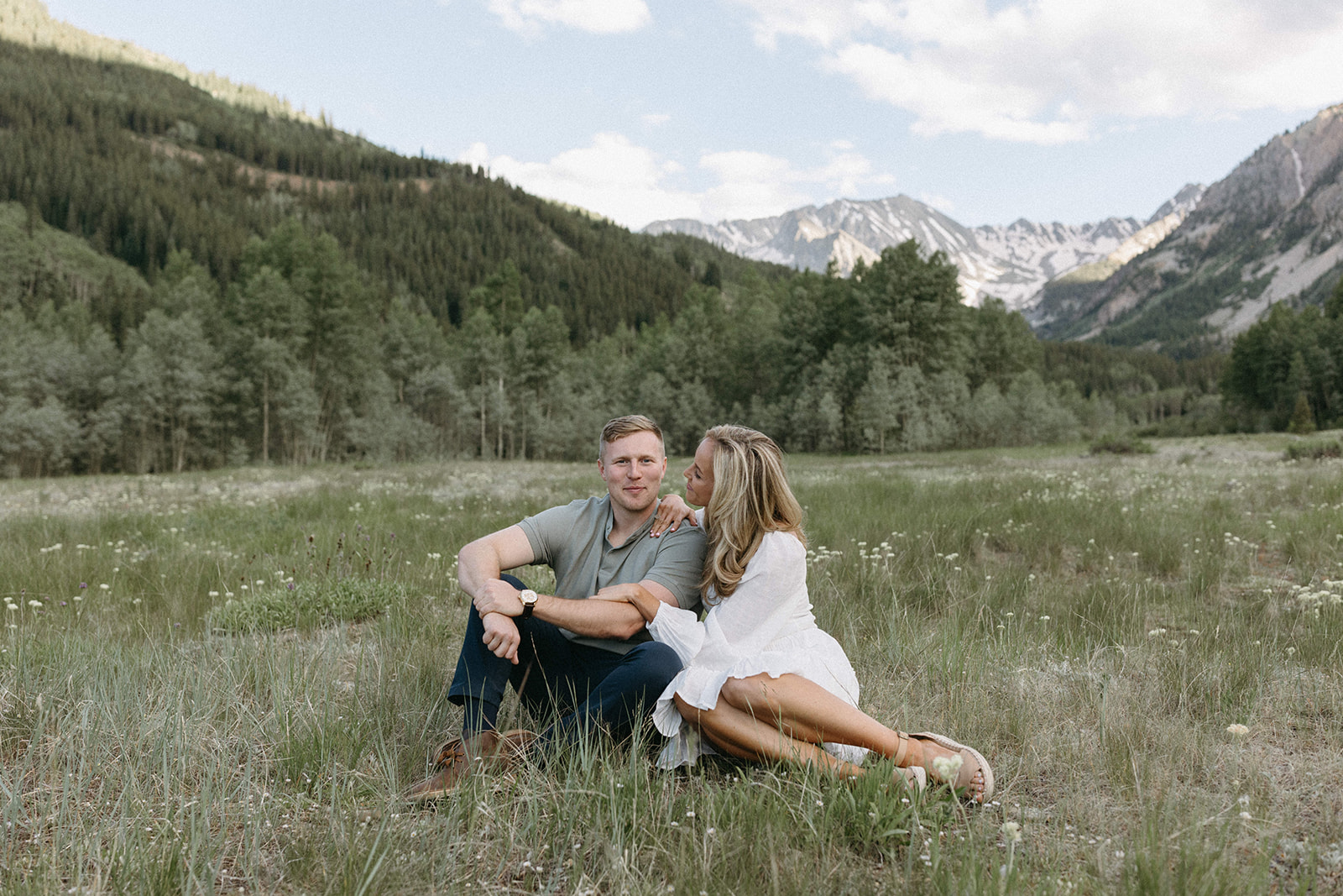 An elevated engagement couple sits in a wildflower meadow during their Aspen engagement session at Sunset. 