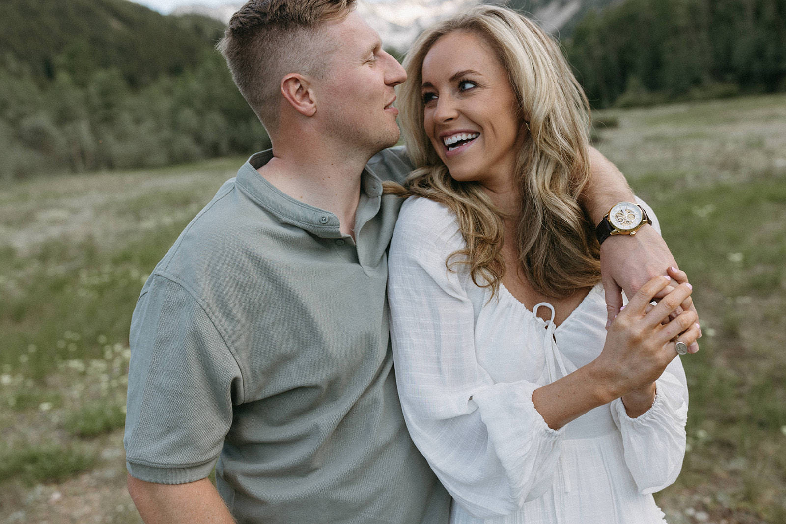 A man in a forest green polo shirt embraces his fiancée in a wildflower meadow during their Aspen engagement session.