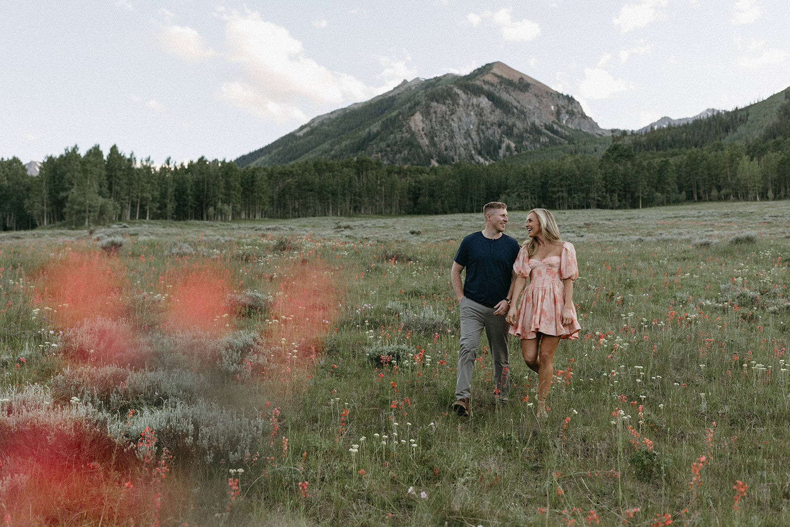 An engaged couple walks through a wildflower meadow in Aspen during their Colorado engagement session. 