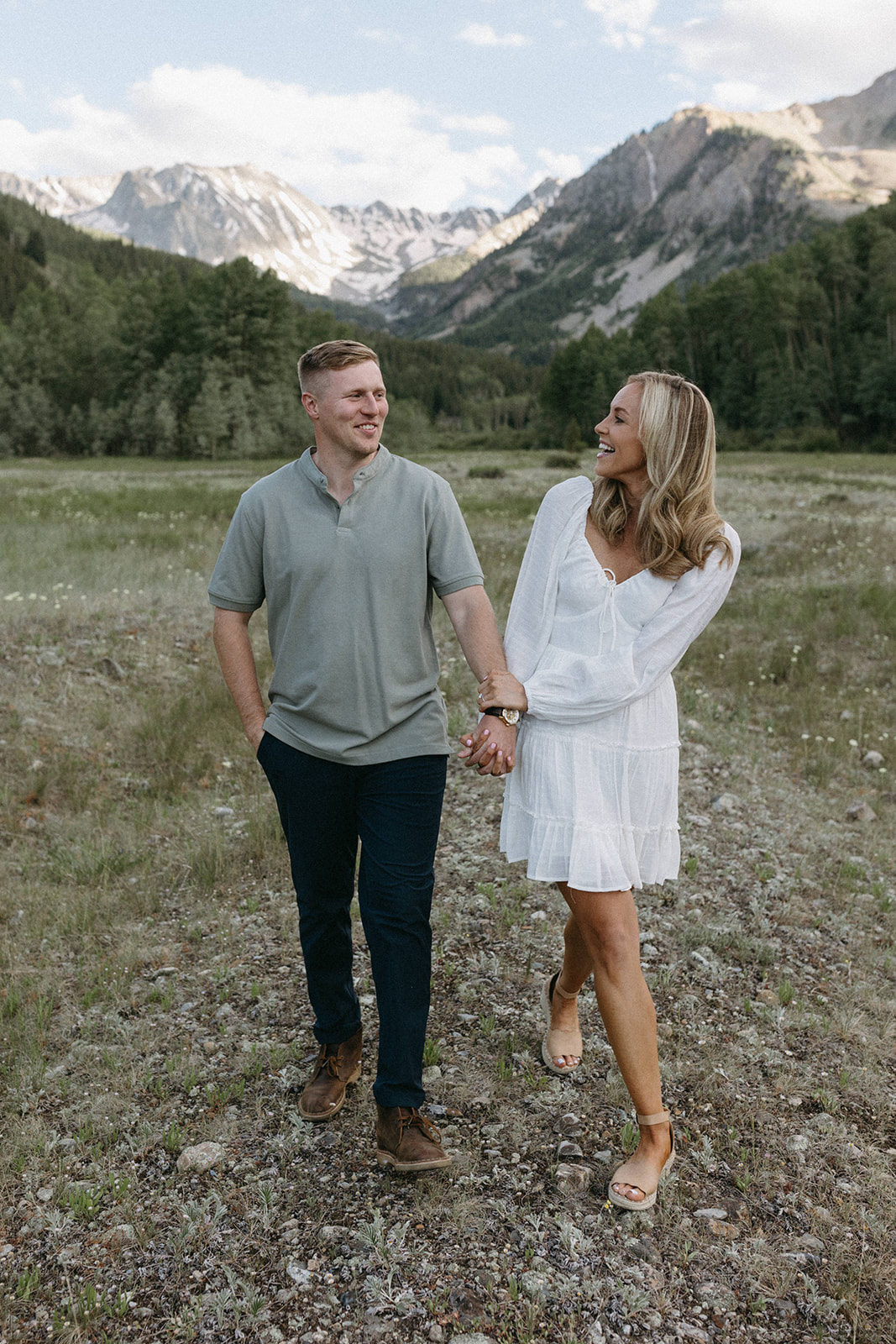 A couple holds hands in a wildflower meadow during their Aspen engagement session in the Colorado Rockies. 