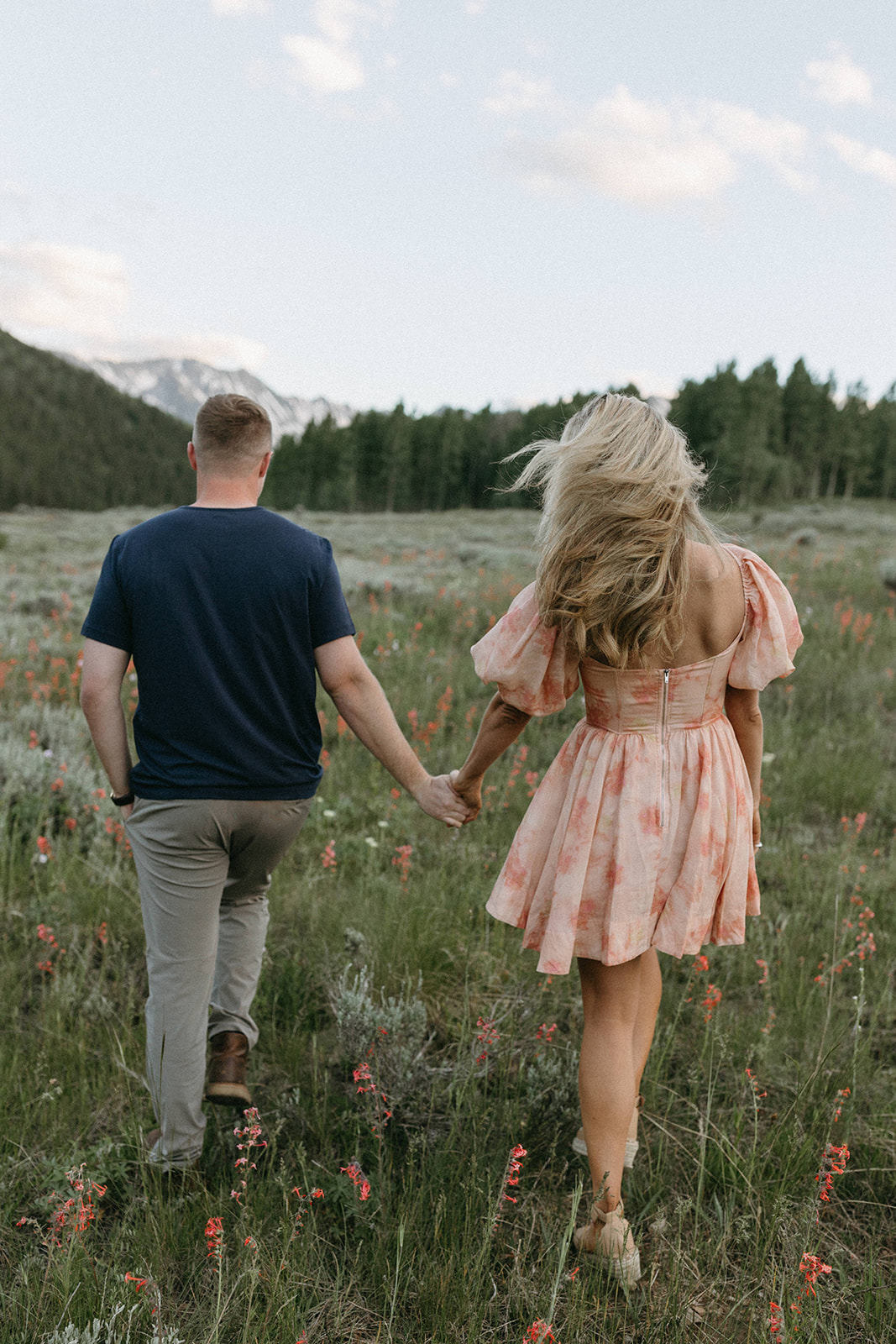 An engaged holds hands while walking through a wildflower meadow during their Aspen engagement session. 