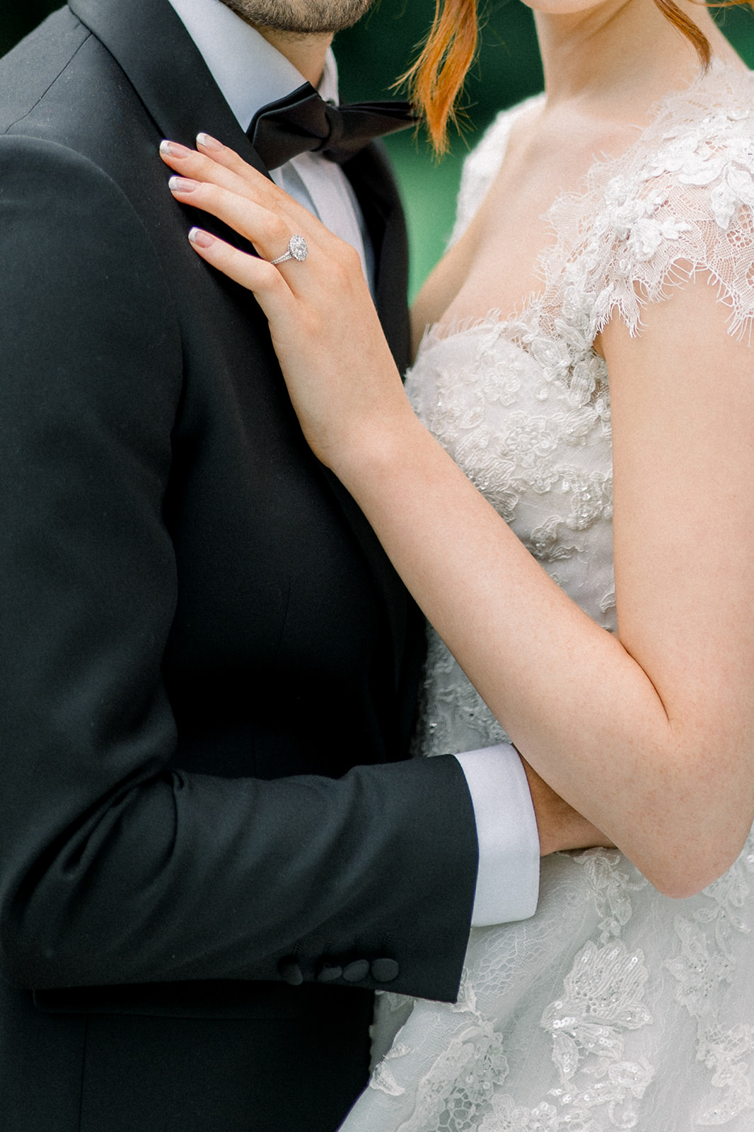 Close-up of a couple's intimate embrace, with focus on the bride's lace sleeve and the groom's black bow tie.