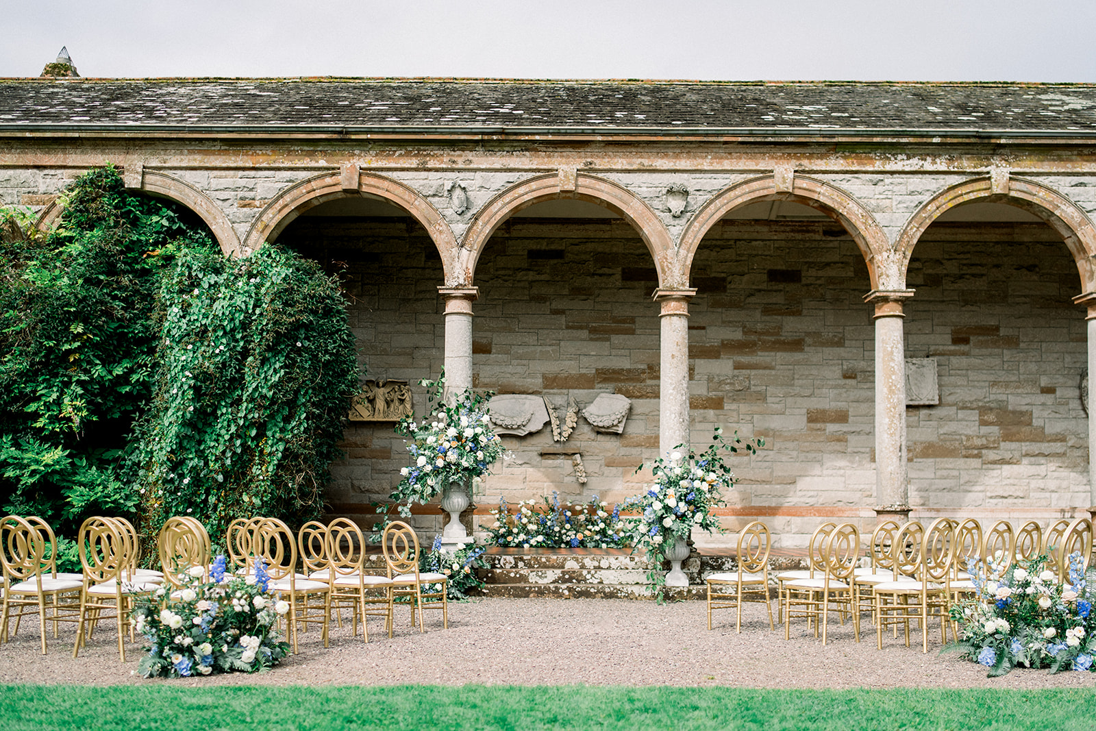 Stone-arched ceremony at Castle Leslie, Ireland with gold chairs and luxurious blue florals