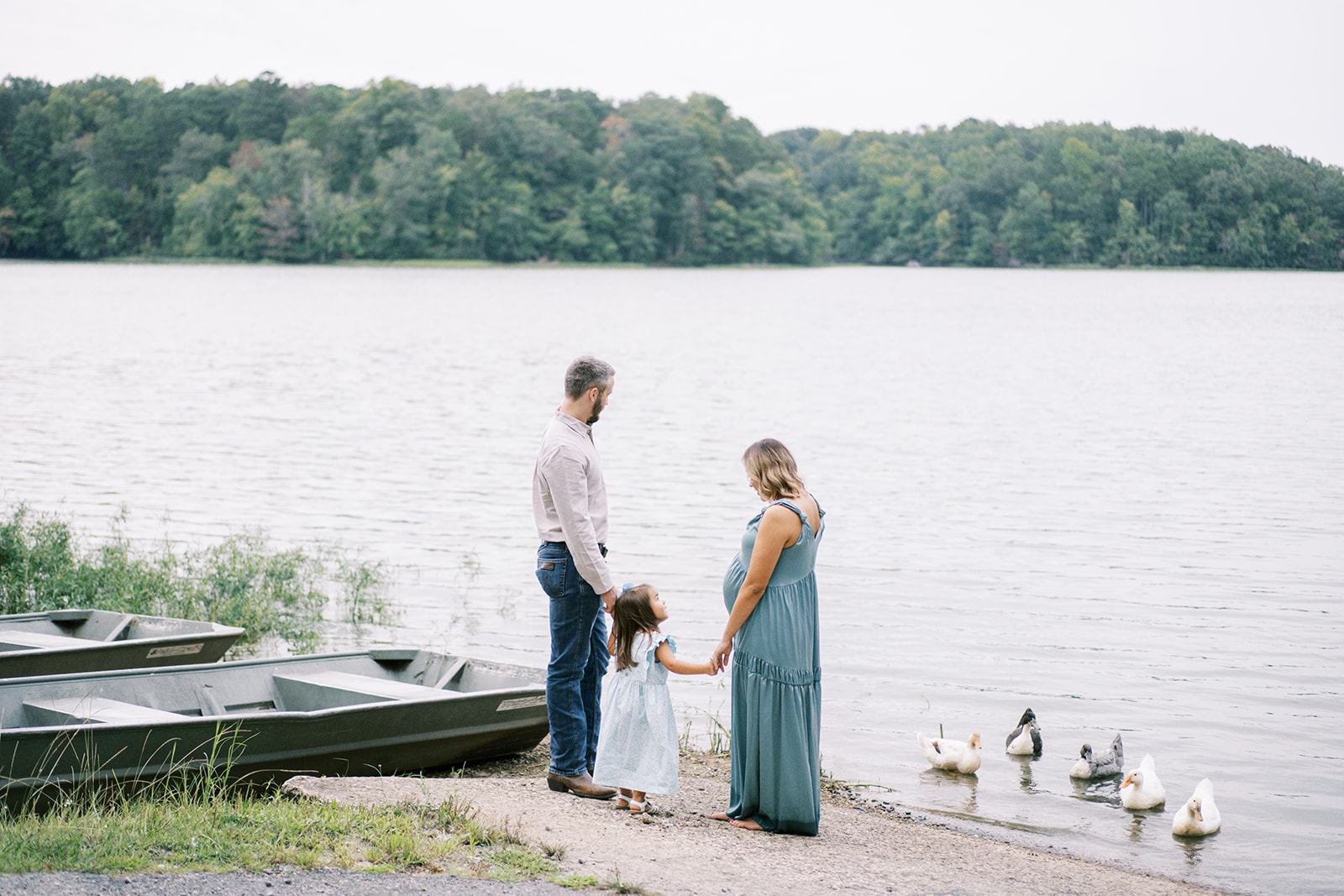 A family looks out at the lake near some boats and ducks during a family maternity session by Kelsey Dawn Photography
