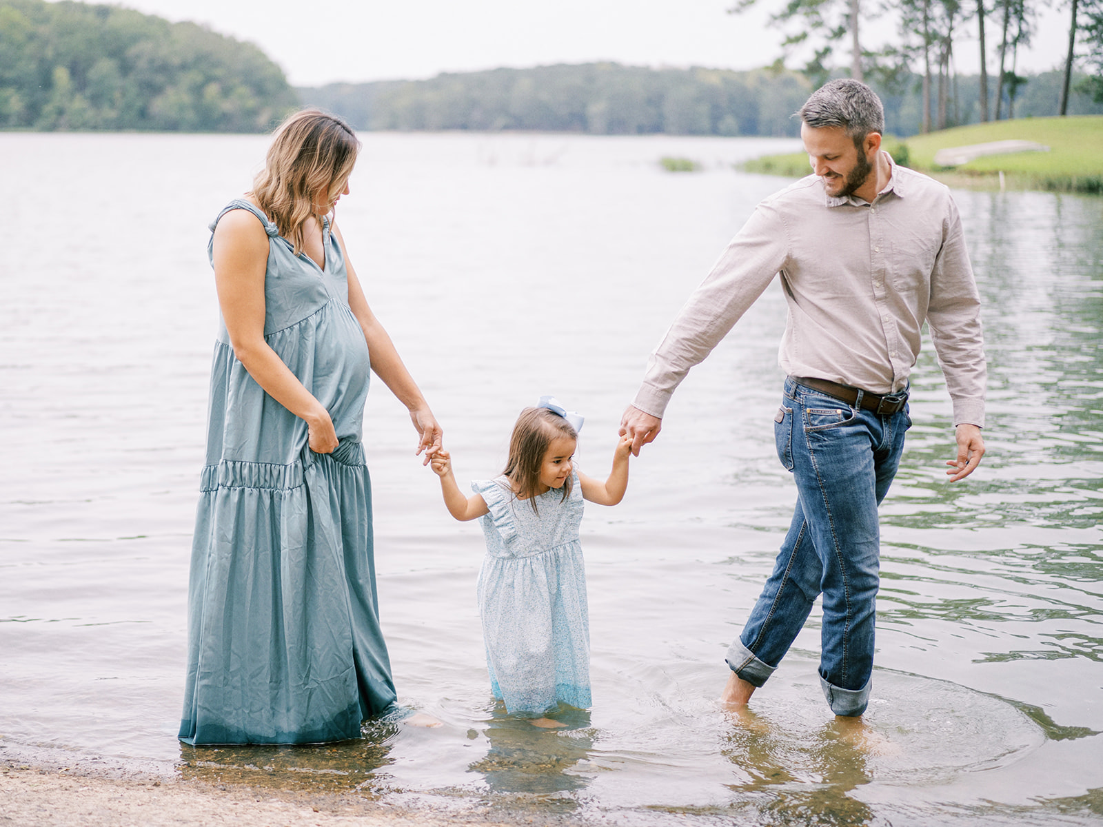 A family walks through the water in a lake during a family maternity session by Kelsey Dawn Photography