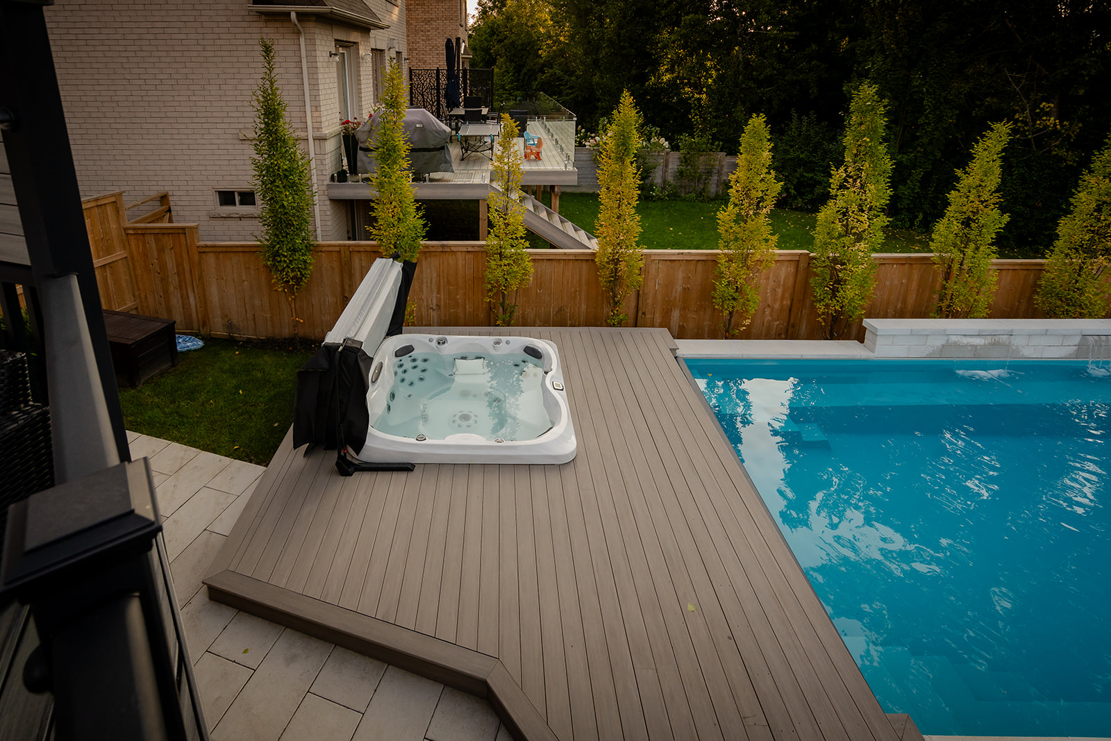 A jacuzzi surrounded by a raised deck and an inground pool on the right.